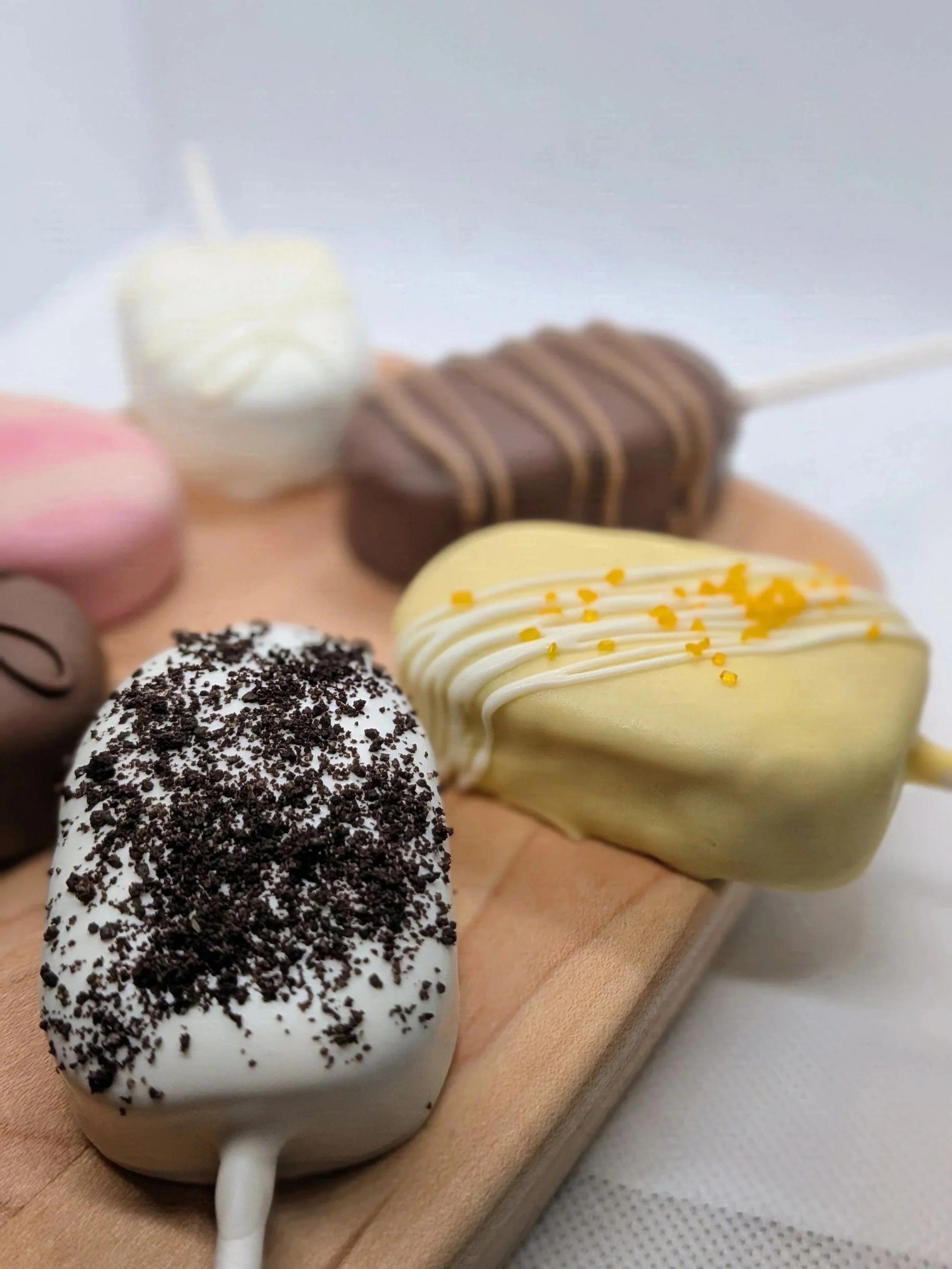 Close-up of a variety of decorated cakesicles on a wooden surface.
