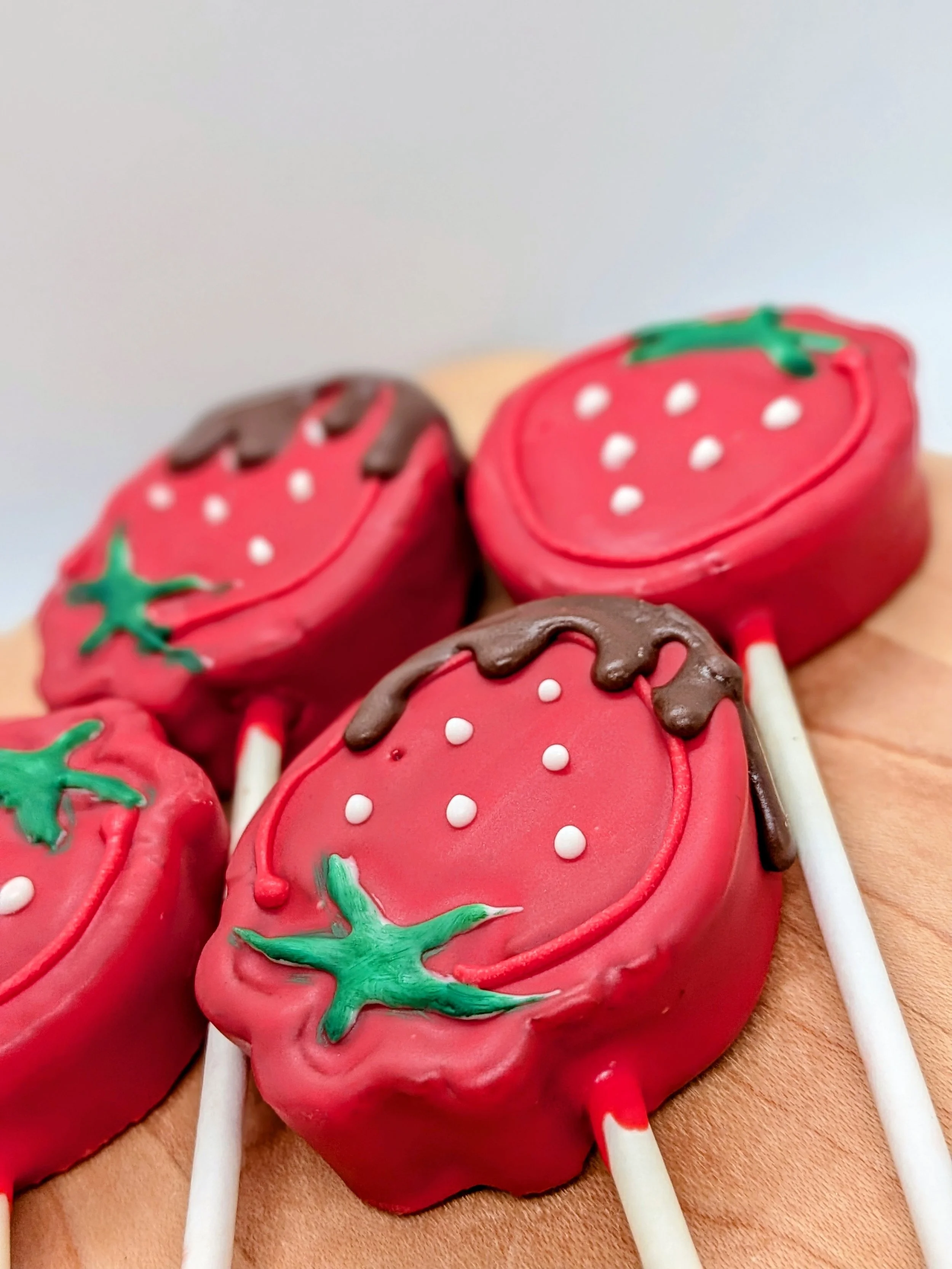 Close-up of strawberry-shaped cake pops decorated with red, green, white, and chocolate icing.