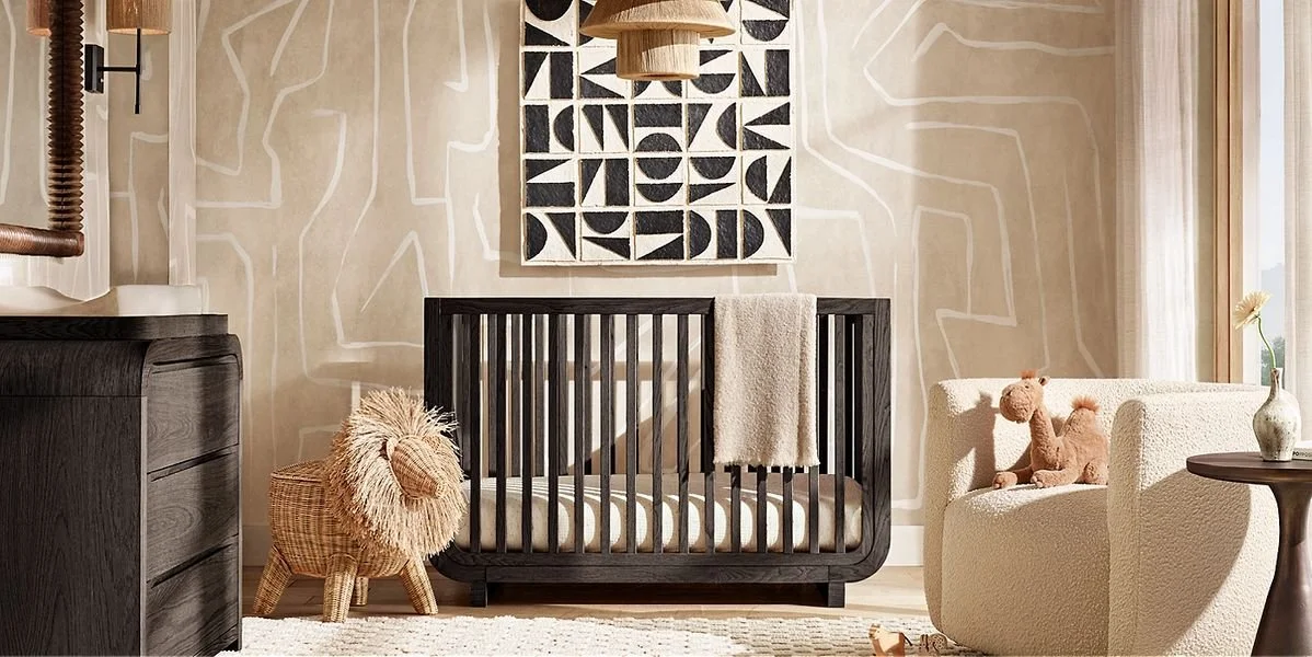Nursery room with crib, stuffed animal lion, armchair with stuffed camel, basket, dresser, side table with vase and flower, wall art, and window.