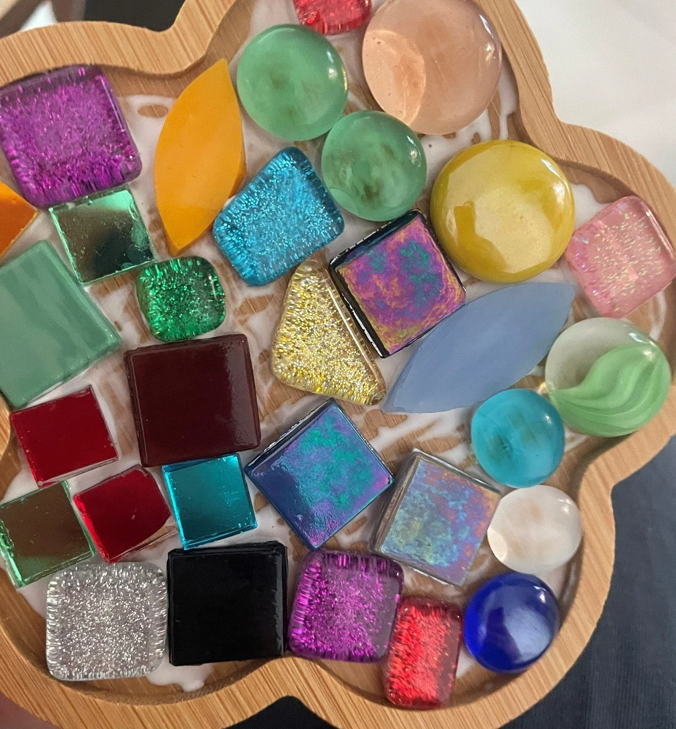 Verschiedene bunte Glassteine und Glasperlen auf einem Holztablett.