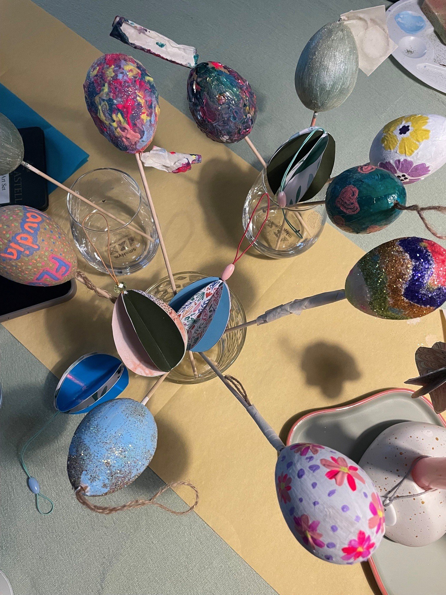 Bunte bemalte Eier auf einem Tisch, umgeben von Kunstmaterialien, vermutlich für eine Osterdekoration oder -aktivität.
