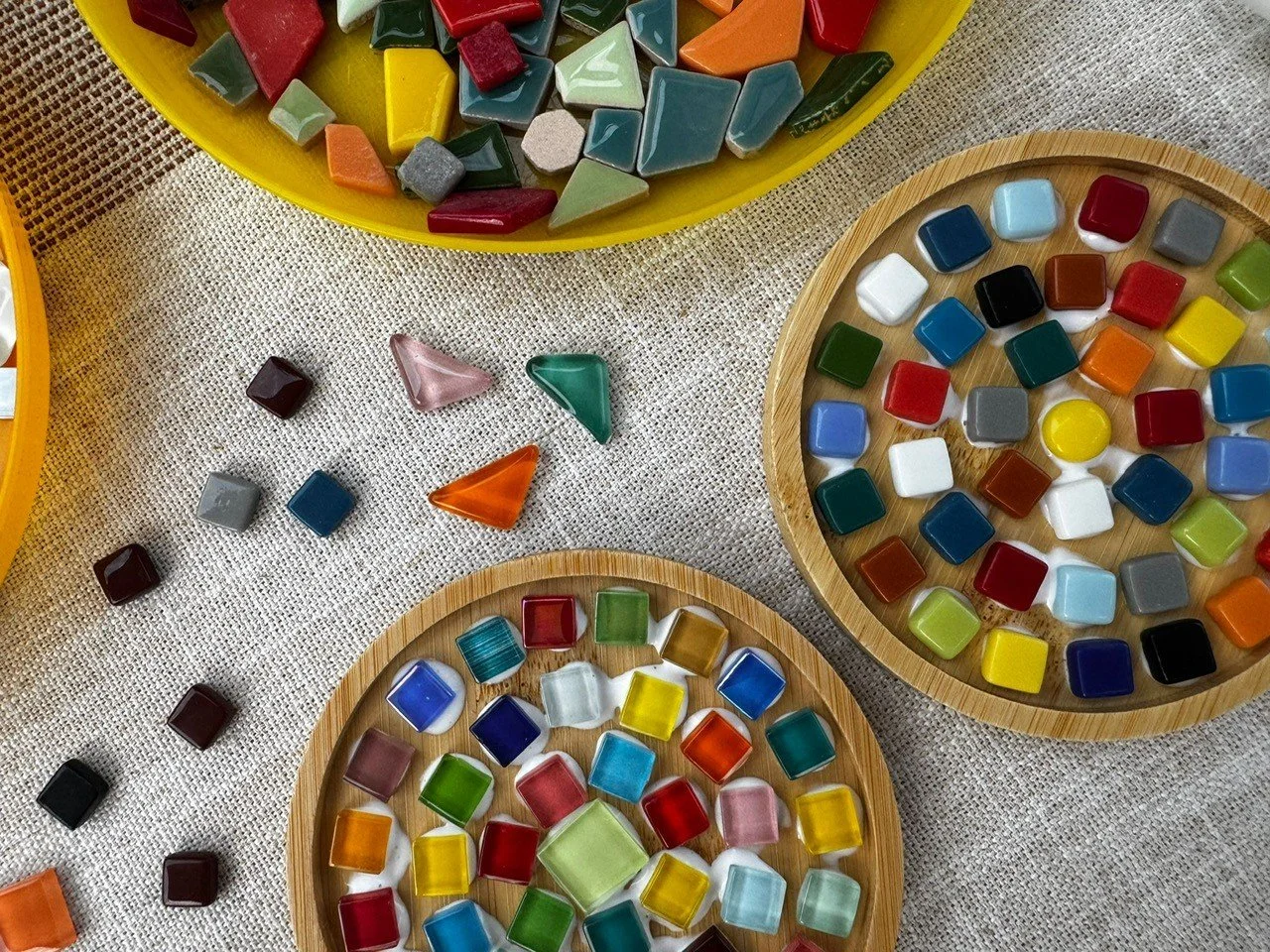 Bunte Glassteine in verschiedenen Farben und Formen auf Holztellern und einer Stoffoberfläche