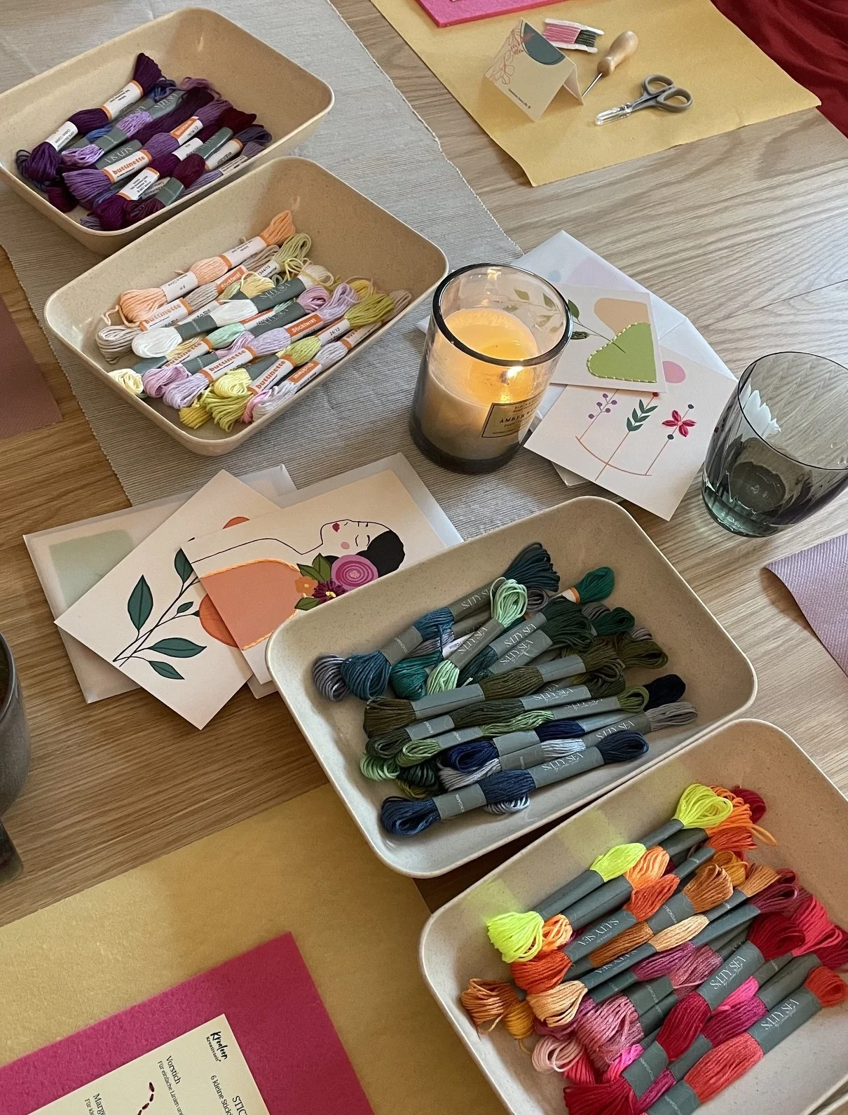 Fünf hübsch gestaltete Grußkarten mit floralen und abstrakten Stickereien, dekoriert mit Salbei, Eukalyptus, getrockneten Blumen und Goldakzenten, auf einem hellen Stoffhintergrund, umgeben von Stickgarn, Schere und getrockneten Blumen.