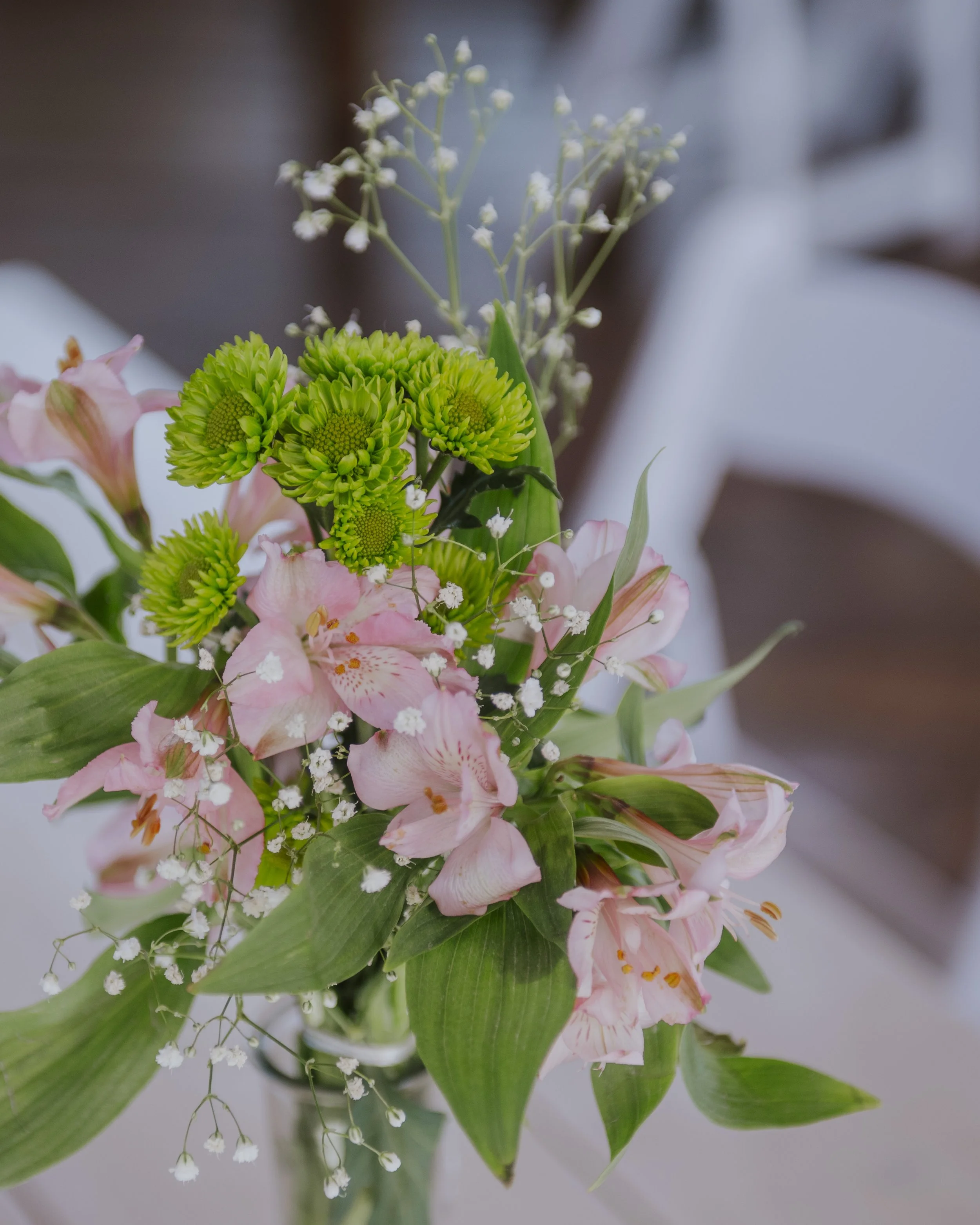 Close-up of a flower bouquet with pink lilies, green chrysanthemums, white baby's breath, and various green leaves.