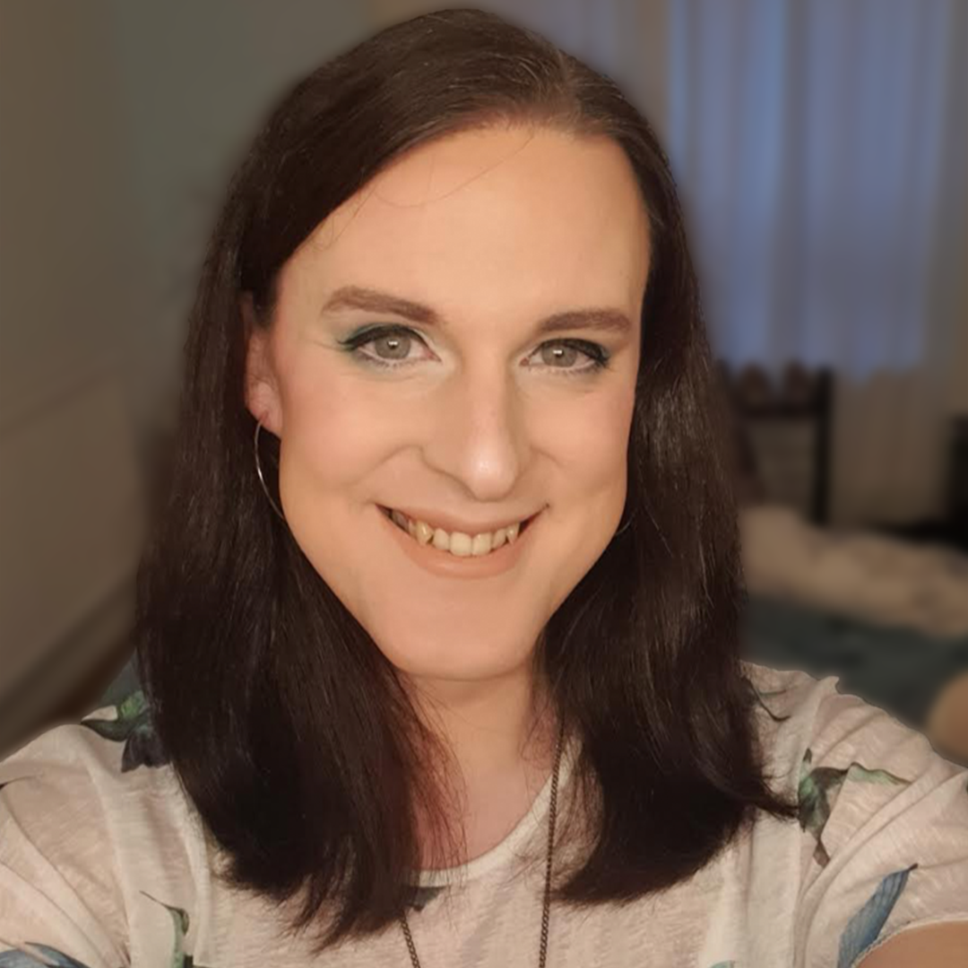 Close-up of Samantha Webb smiling with brown shoulder-length hair, wearing light makeup, silver hoop earrings, and a white t-shirt.