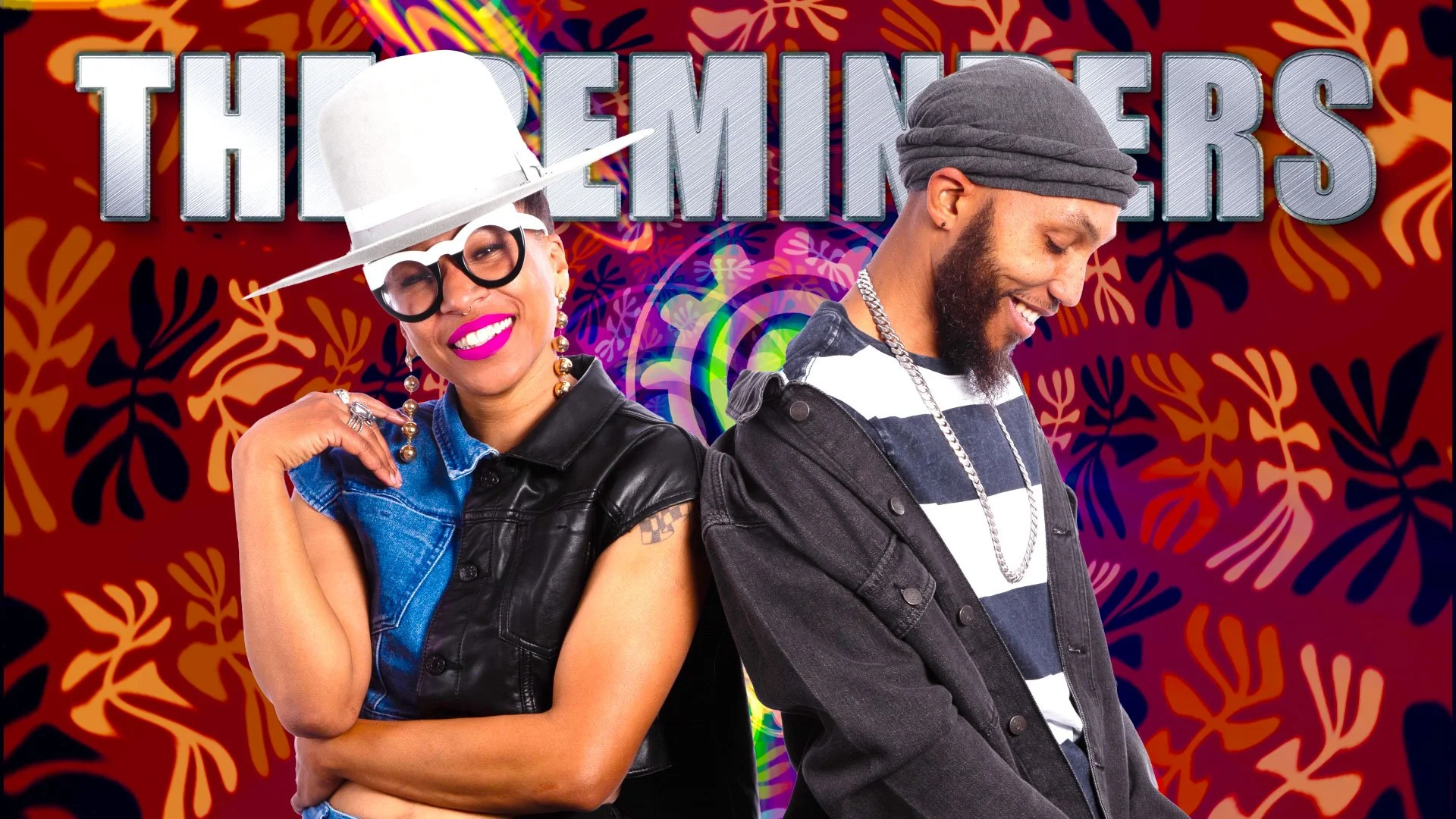 Two people standing back to back against a colorful patterned background with the word 'THE EMITTERS' in large silver letters behind them. The woman on the left is smiling, wearing a white hat, black glasses, pink lipstick, earrings, a denim vest, and a tattoo on her arm. The man on the right is smiling, wearing a gray headwrap, a black jacket, and a striped shirt with a silver chain.
