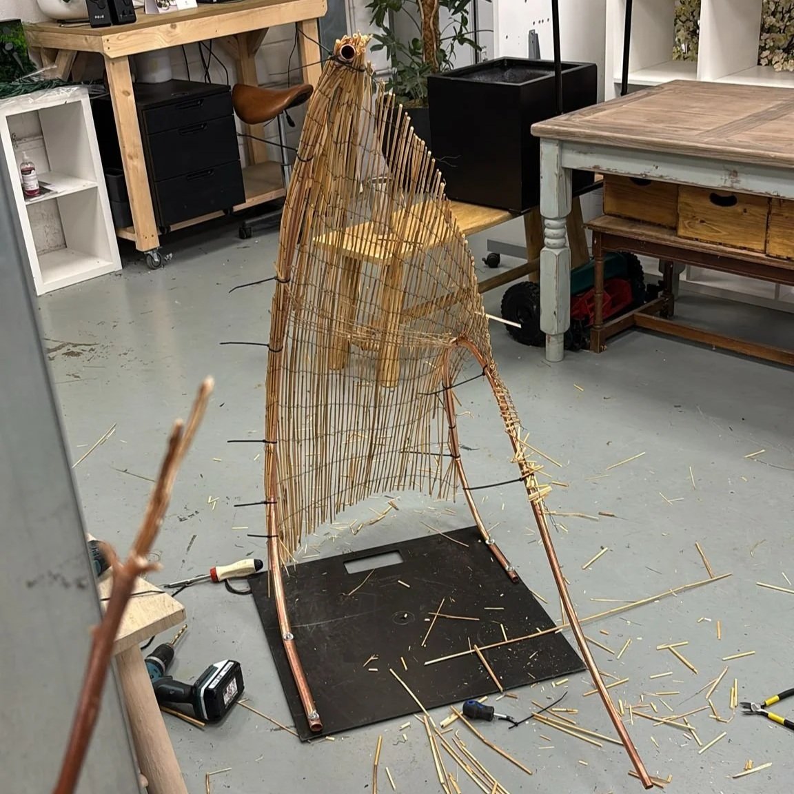 A workshop with a partially built wicker sculpture of a wave, surrounded by tools showing exploratory making.