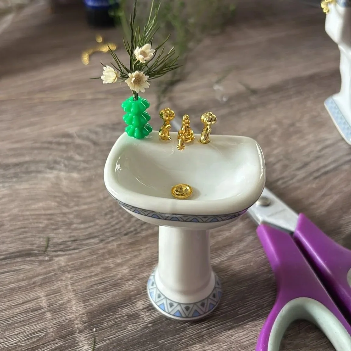 Work in progress photo of a miniature white ceramic sink with a tiny preserved flower display. 