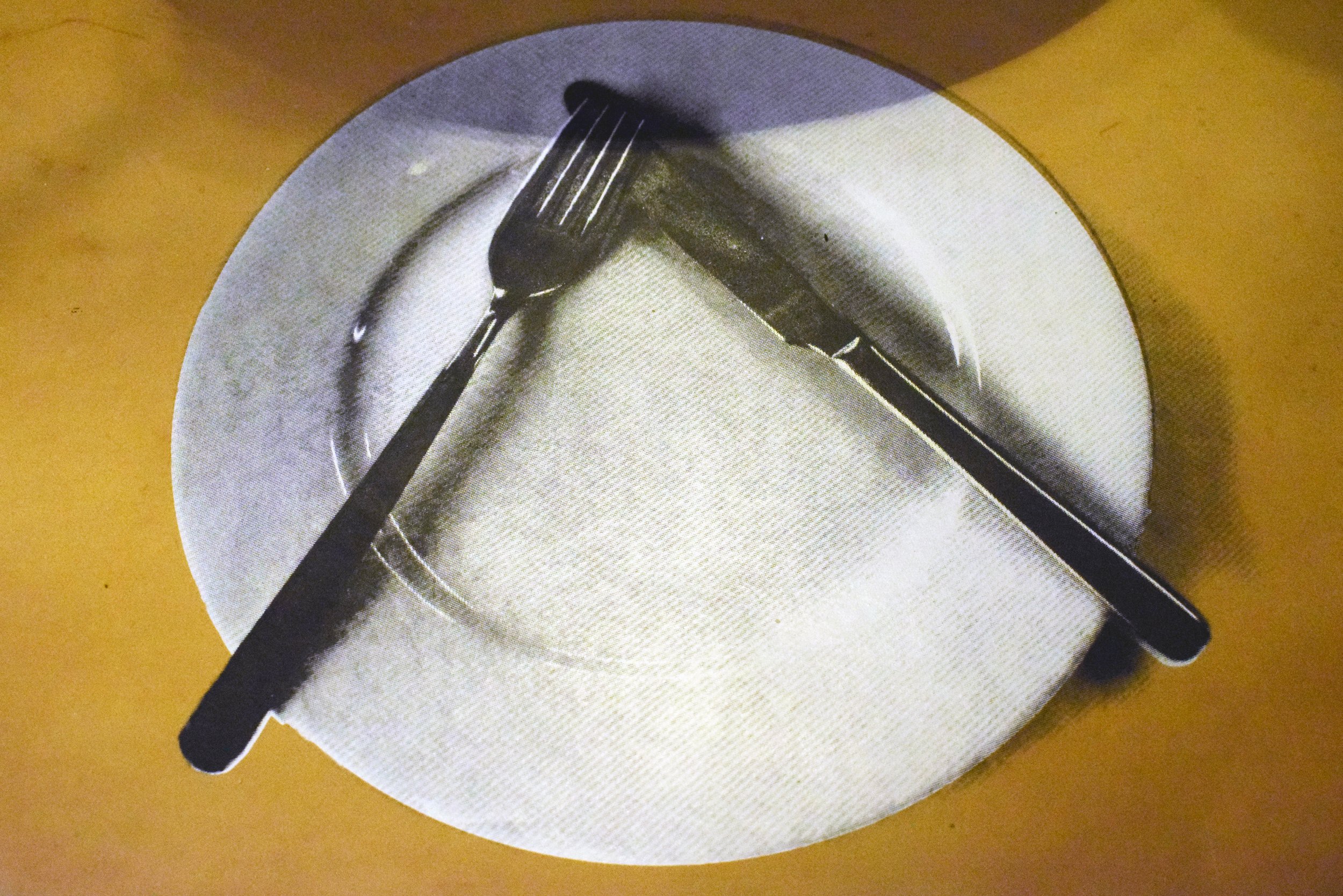 Screen print of a set dining table displayed on a leather tablecloth as part of the immersive installation.