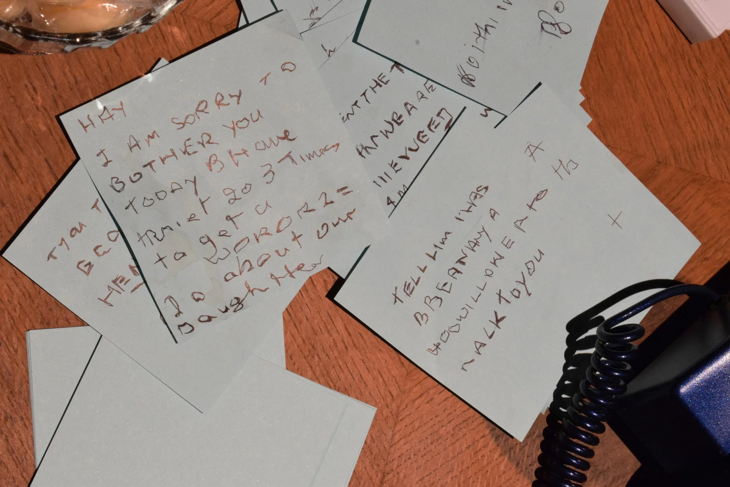 Several handwritten notes on blue paper sheets scattered on a wooden side table as part of an immersive installation.