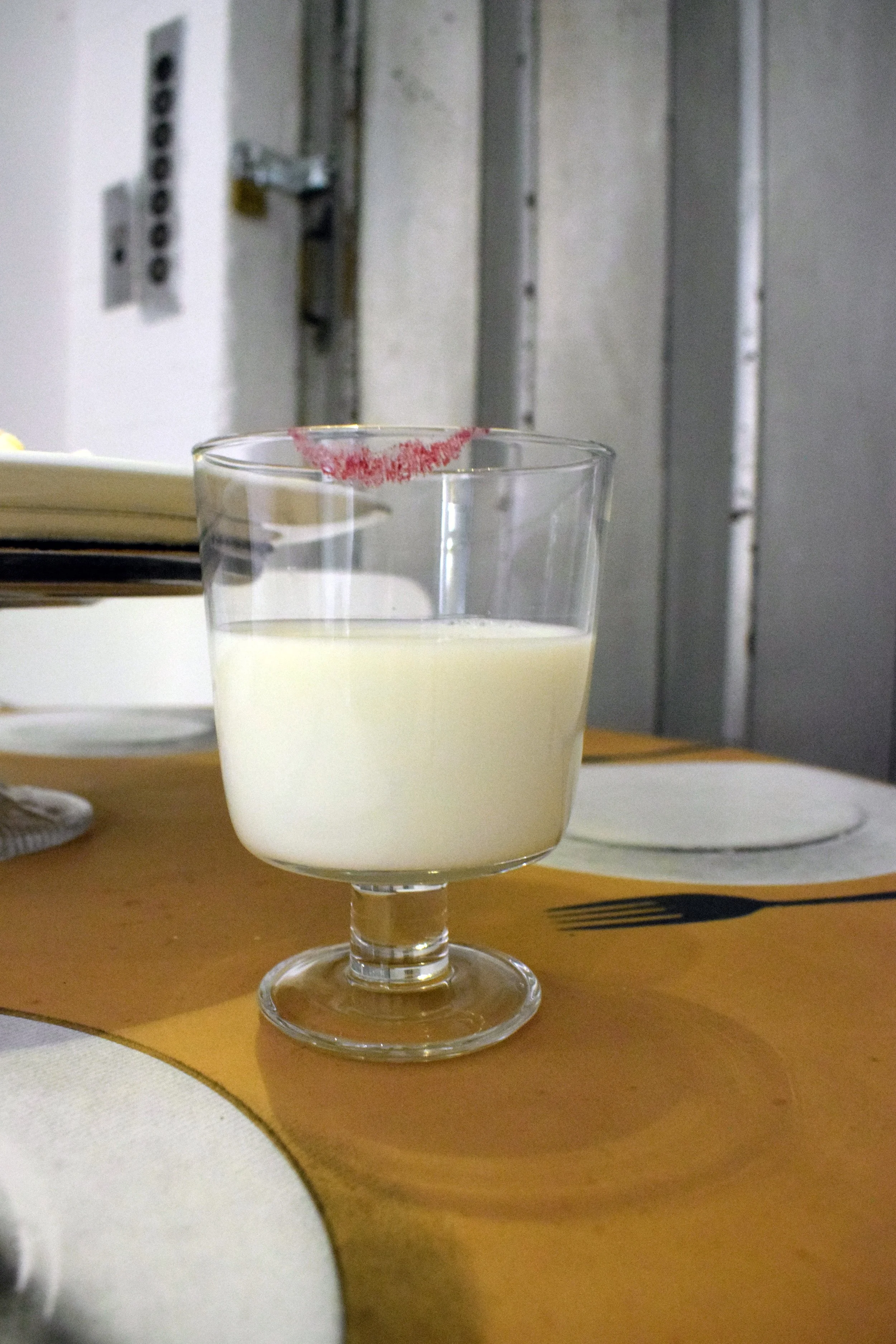 Milk displayed alongside everyday objects containing bovine ingredients, including lipstick, milk sweets and bone china, on a leather tablecloth.