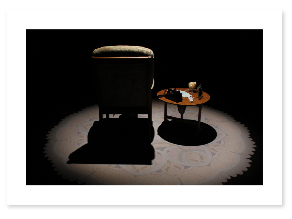 Immersive installation exploring memory and Alzheimer’s, with an armchair and side table illuminated in a darkened room.