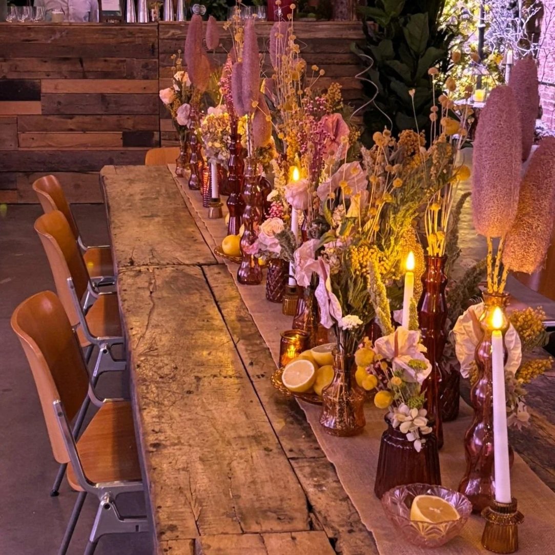 Long communal tablescape styled with preserved and dried flowers, fruit and candles as part of an immersive event experience.
