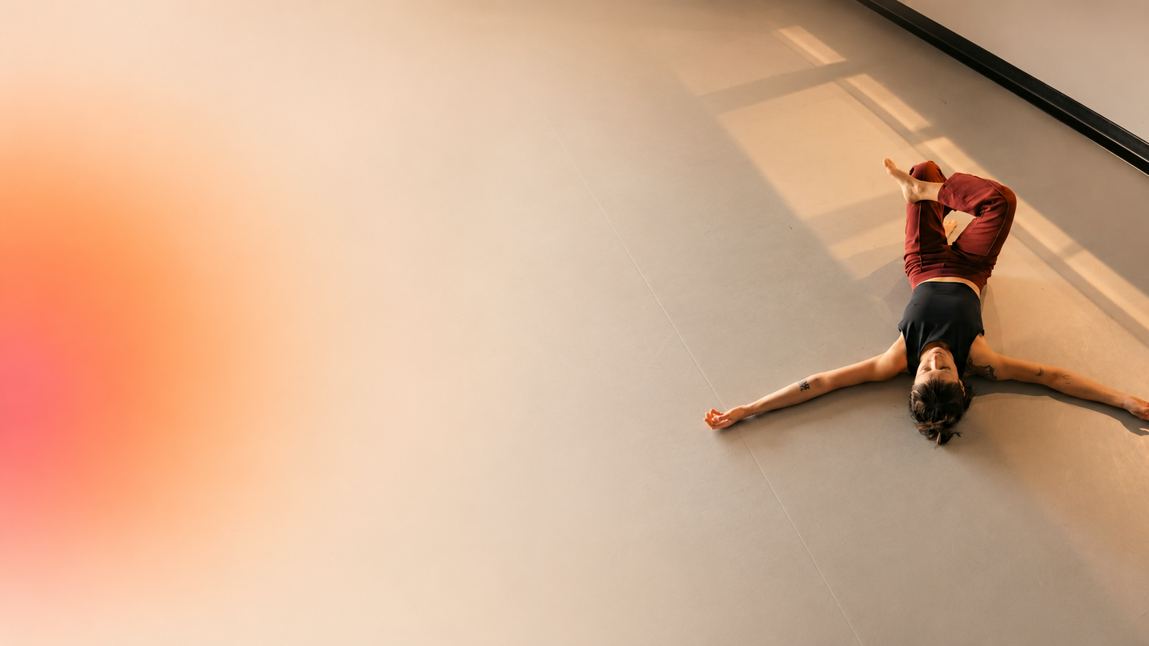 Femme allongée sur le sol, bras étendus, pied en l'air, dans une pièce lumineuse.