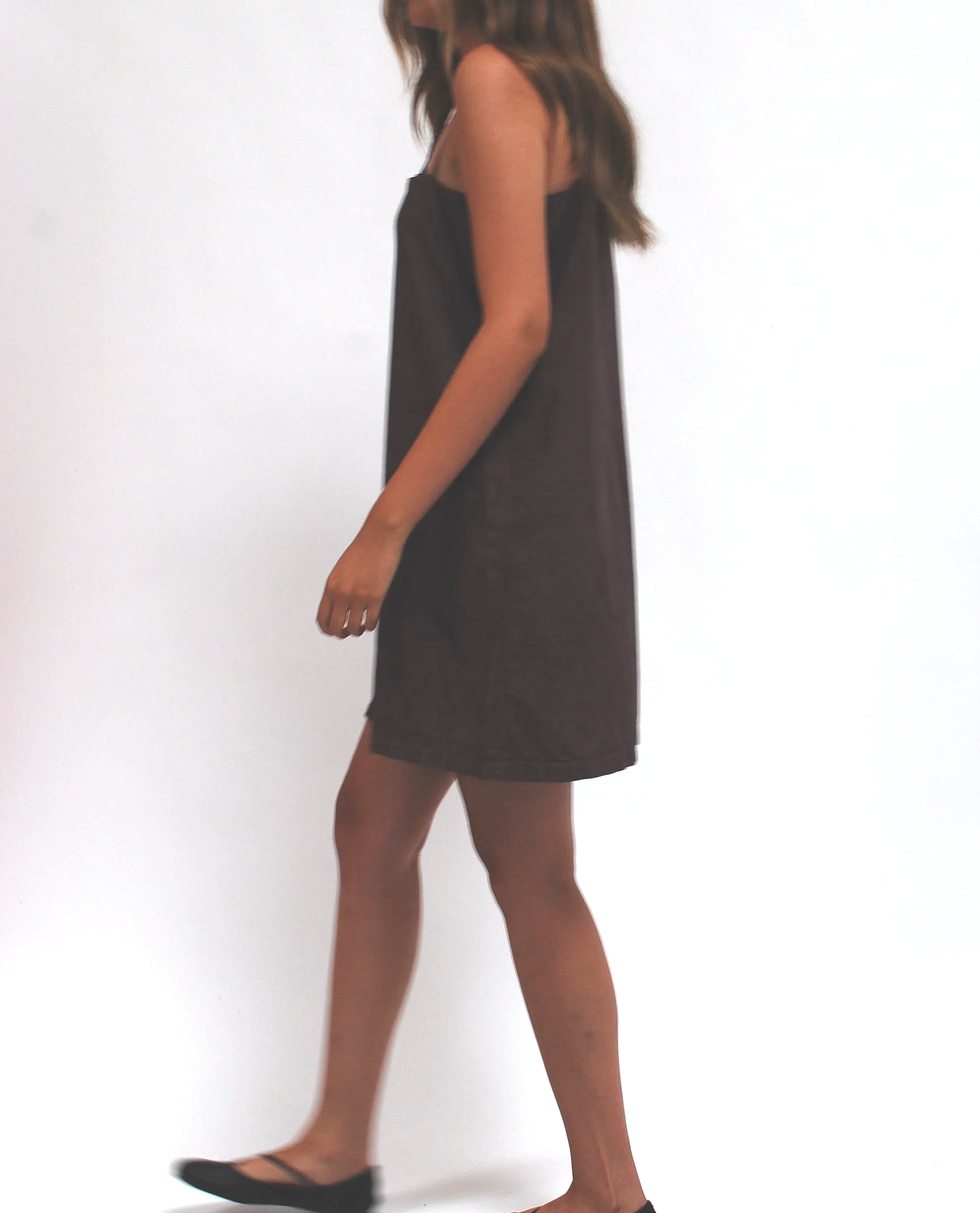A woman standing in black strappy heels, wearing a black slip dress, with her face not visible.