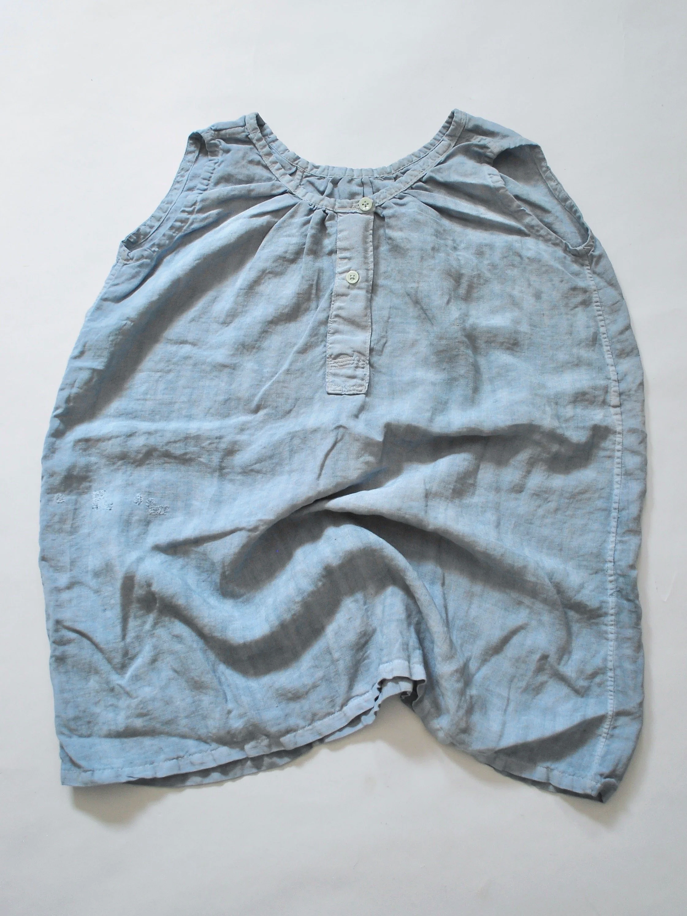 Light blue sleeveless blouse with buttons down the front, lying flat on a white surface.