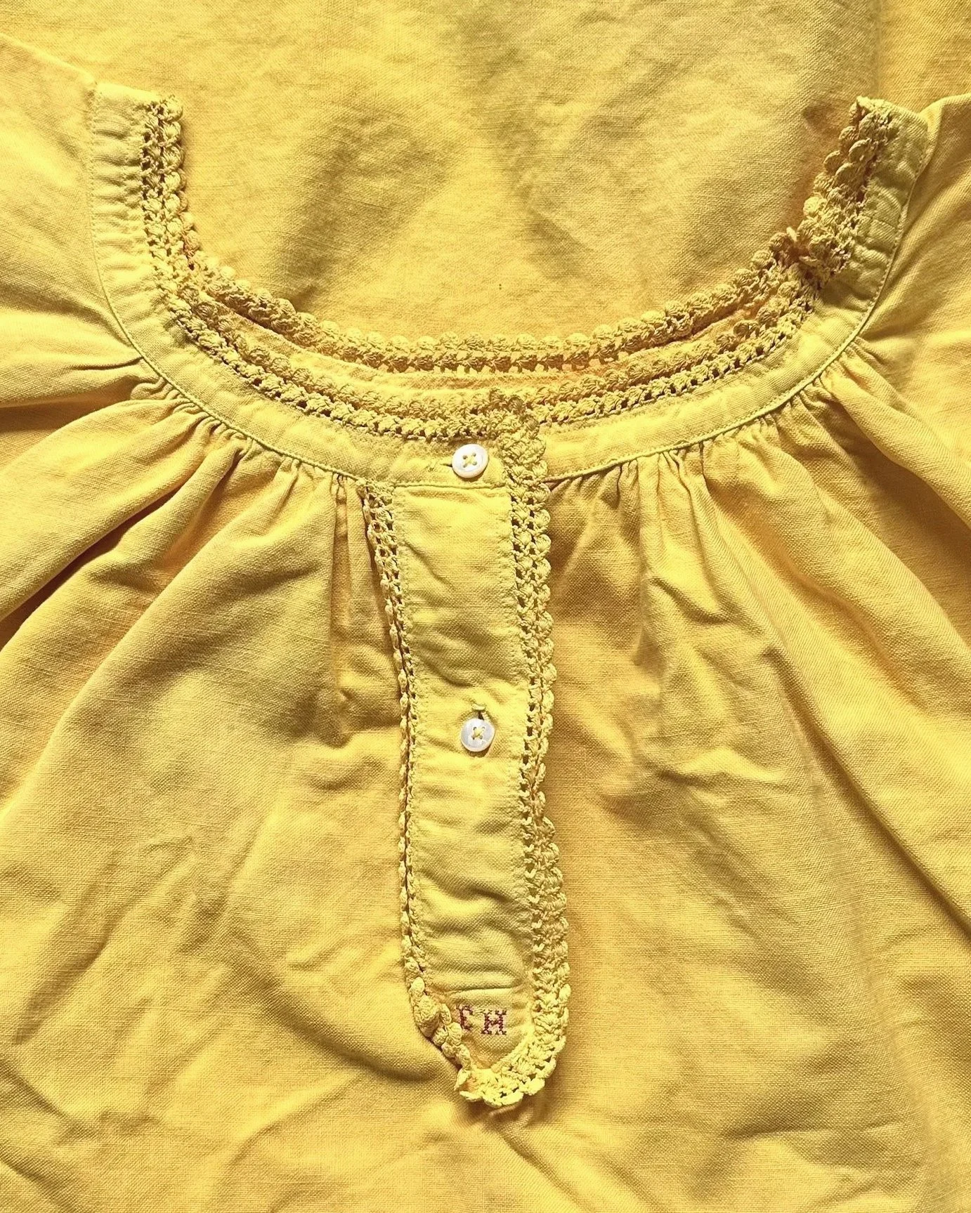 Close-up of a yellow blouse with embroidered details around the collar and button placket.