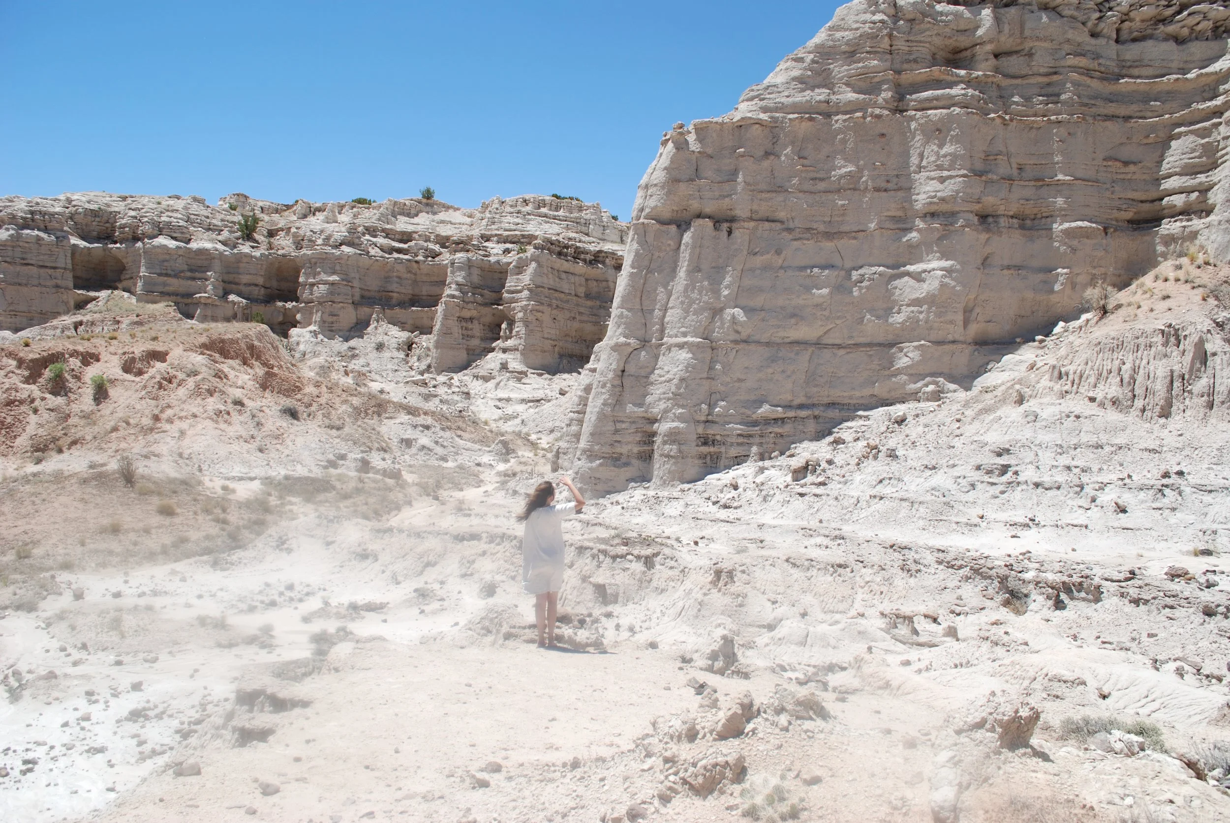 A person taking a photo with a camera or phone in a desert landscape with large white rock formations and a clear blue sky.