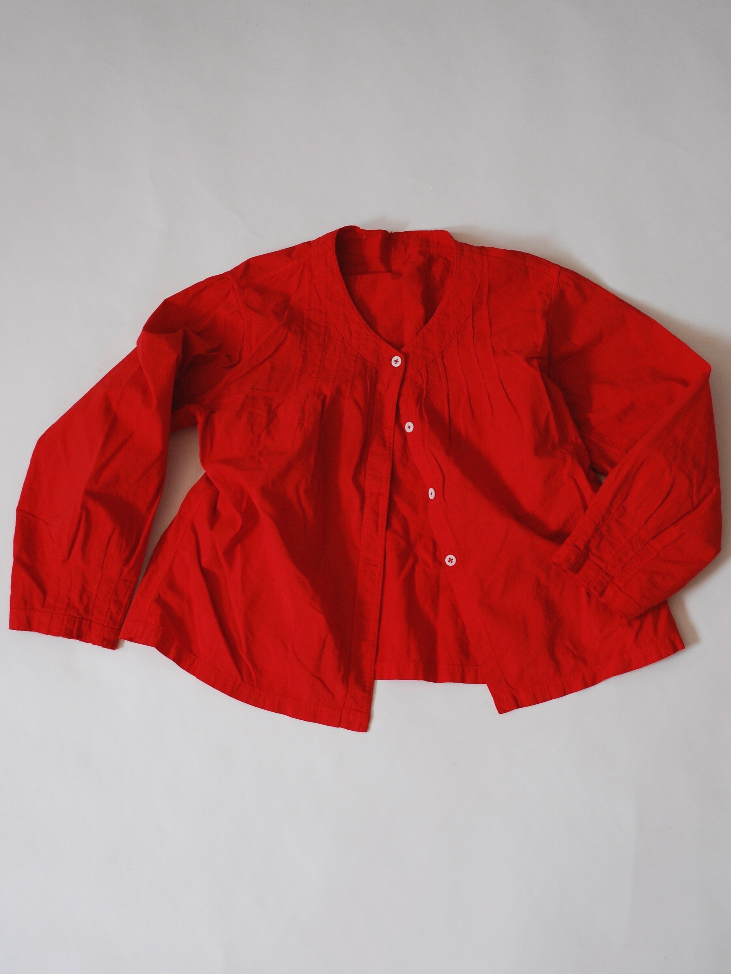 Red long-sleeve shirt with buttons lying flat on a white surface.