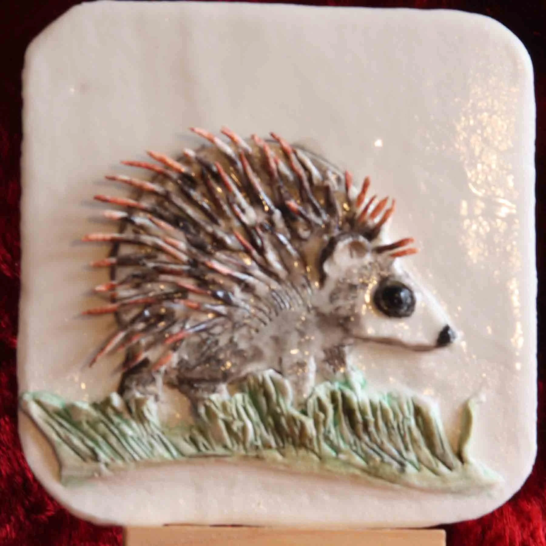 A rectangular ceramic plate with a white background featuring a detailed hedgehog sculpture made of layered ombre green, cream, and brown components.