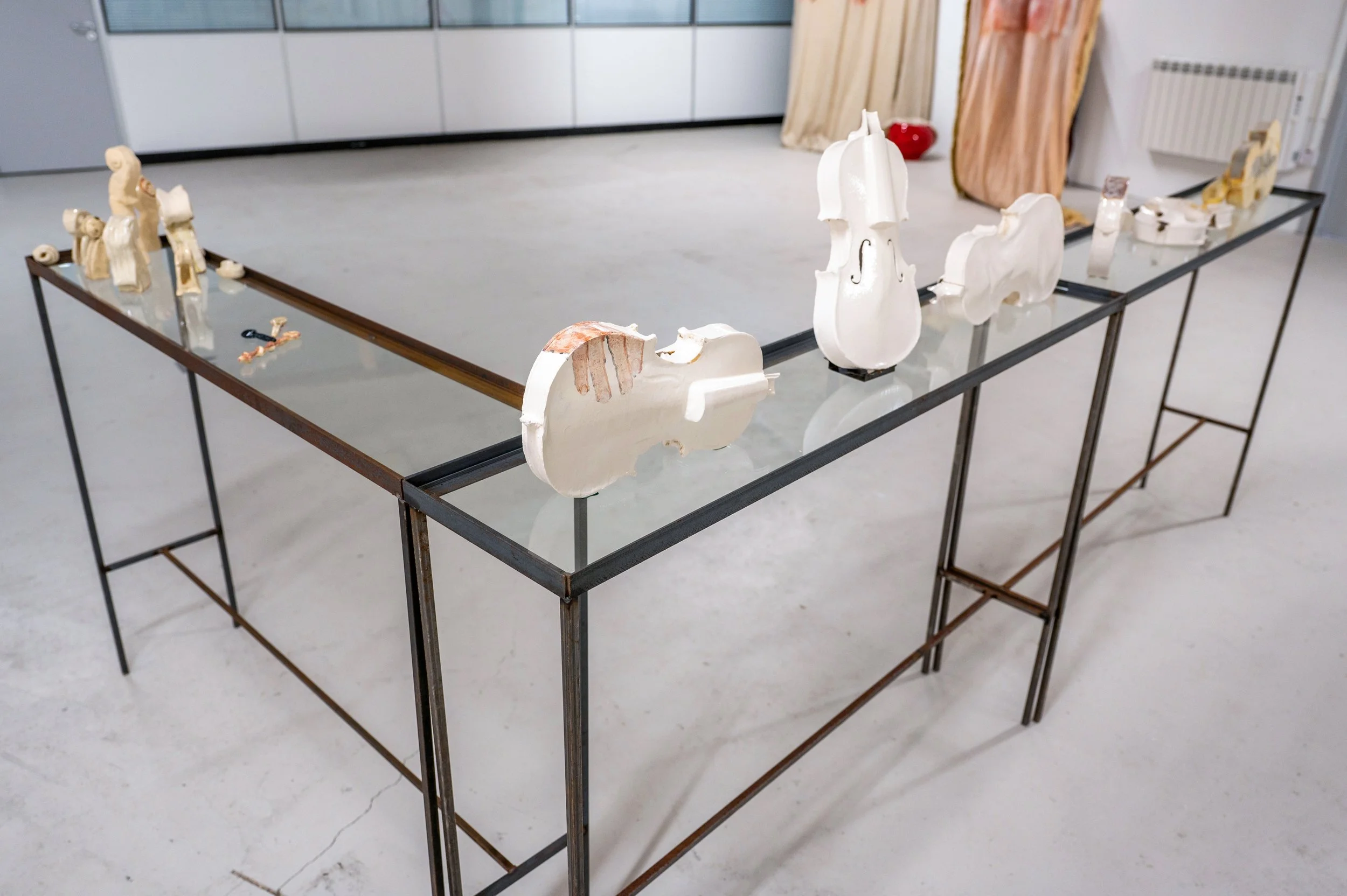 Ceramic sculptures of  white violins, displayed on a metal table in an art gallery or studio.