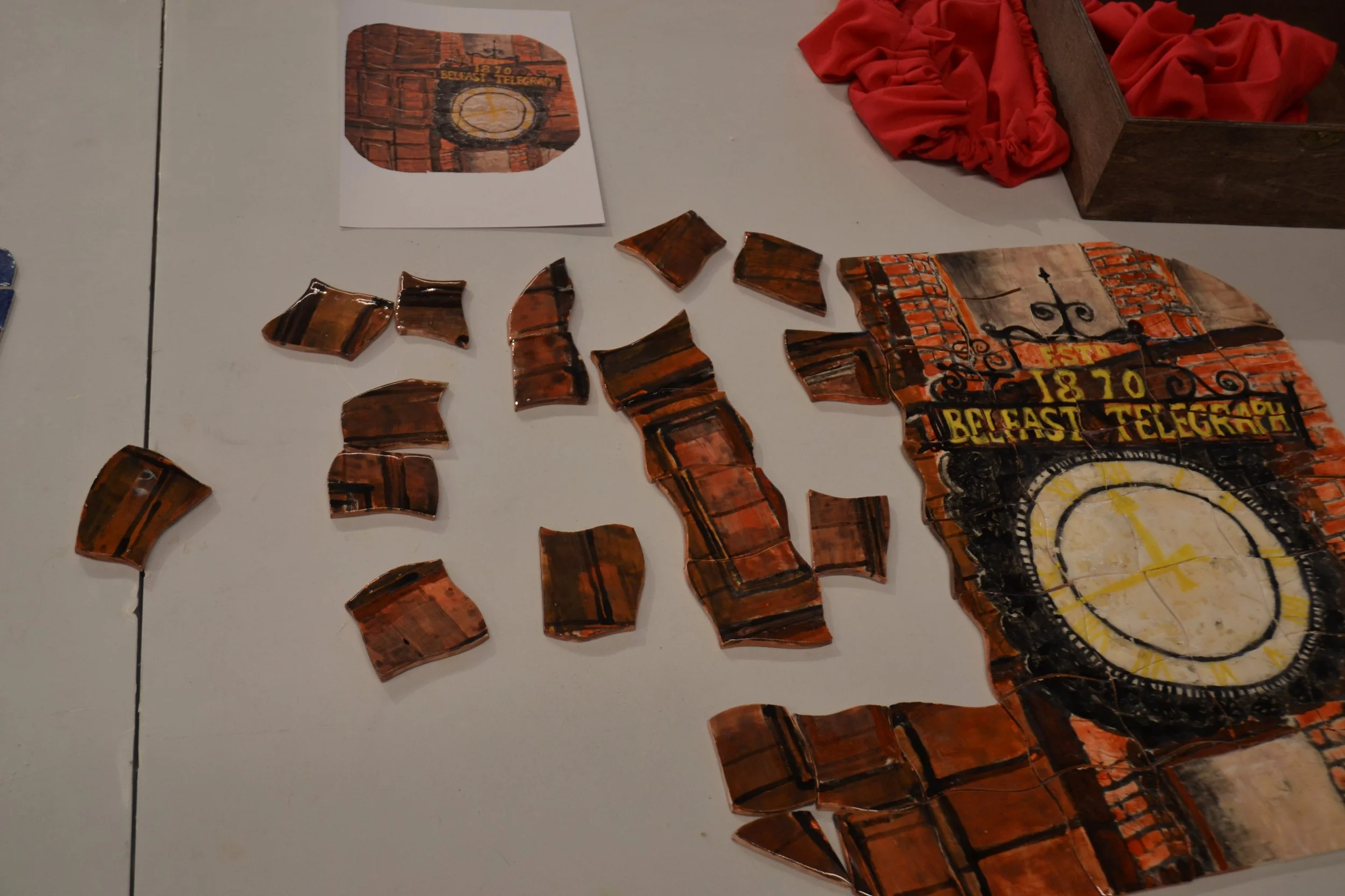 Pieces of broken tiles resembling a brick wall with a sign that reads 'EST. 1870 BELFAST TELEGRAP' and a clock face.