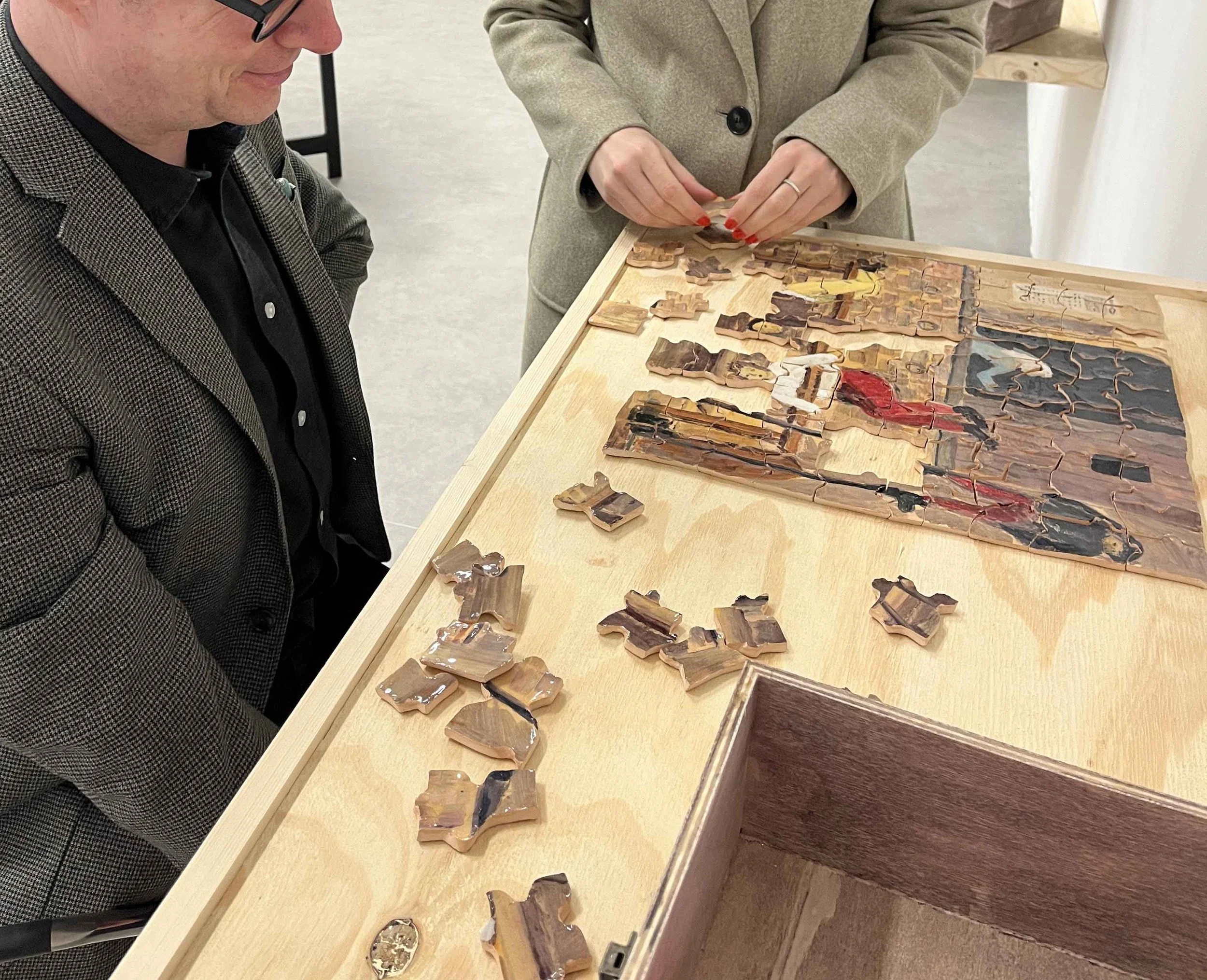 People working on a partially assembled jigsaw puzzle on a wooden table.
