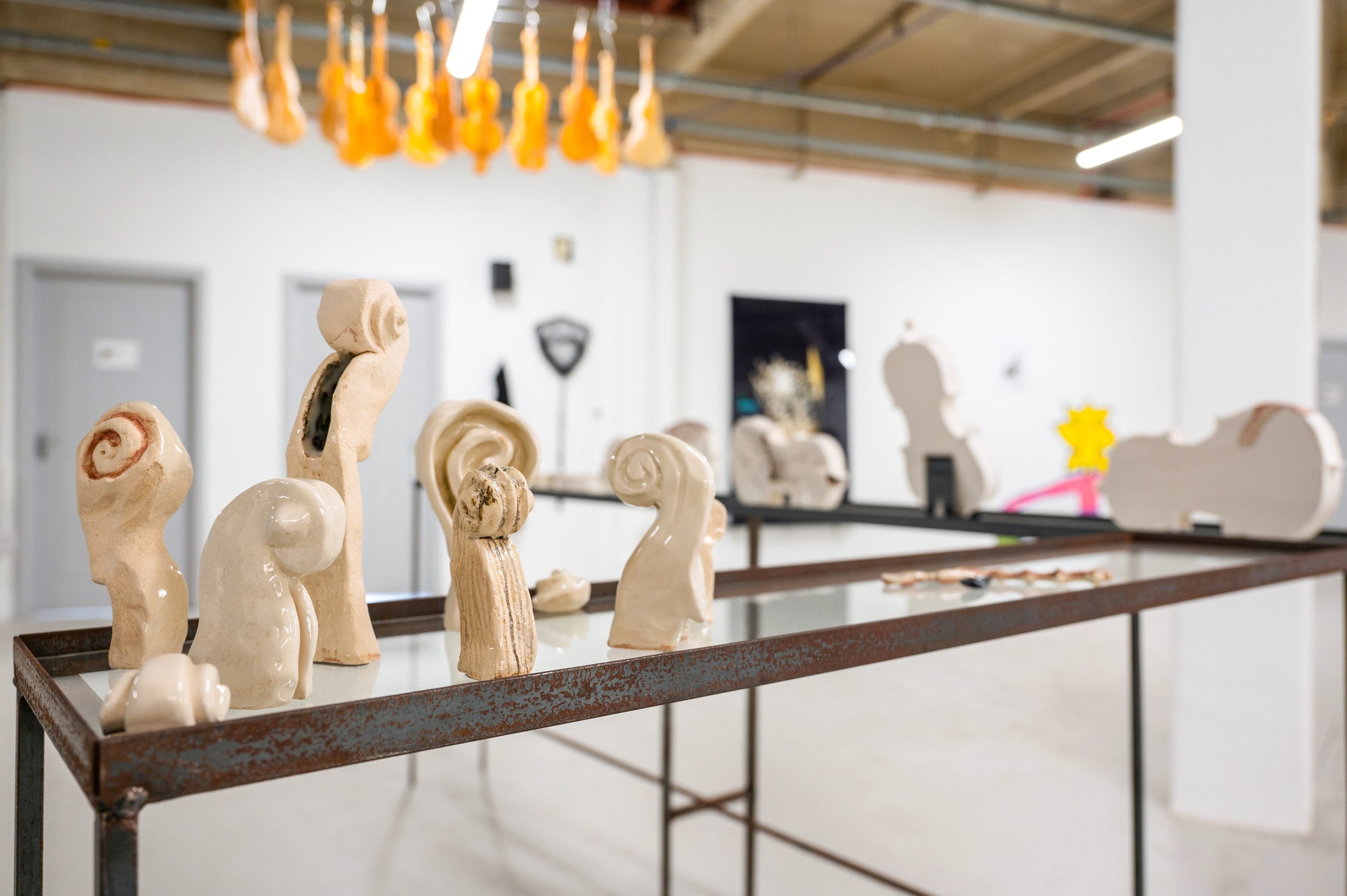 Ceramic sculptures of abstract, spiral and curved shapes displayed on a metal table in an art gallery or studio.