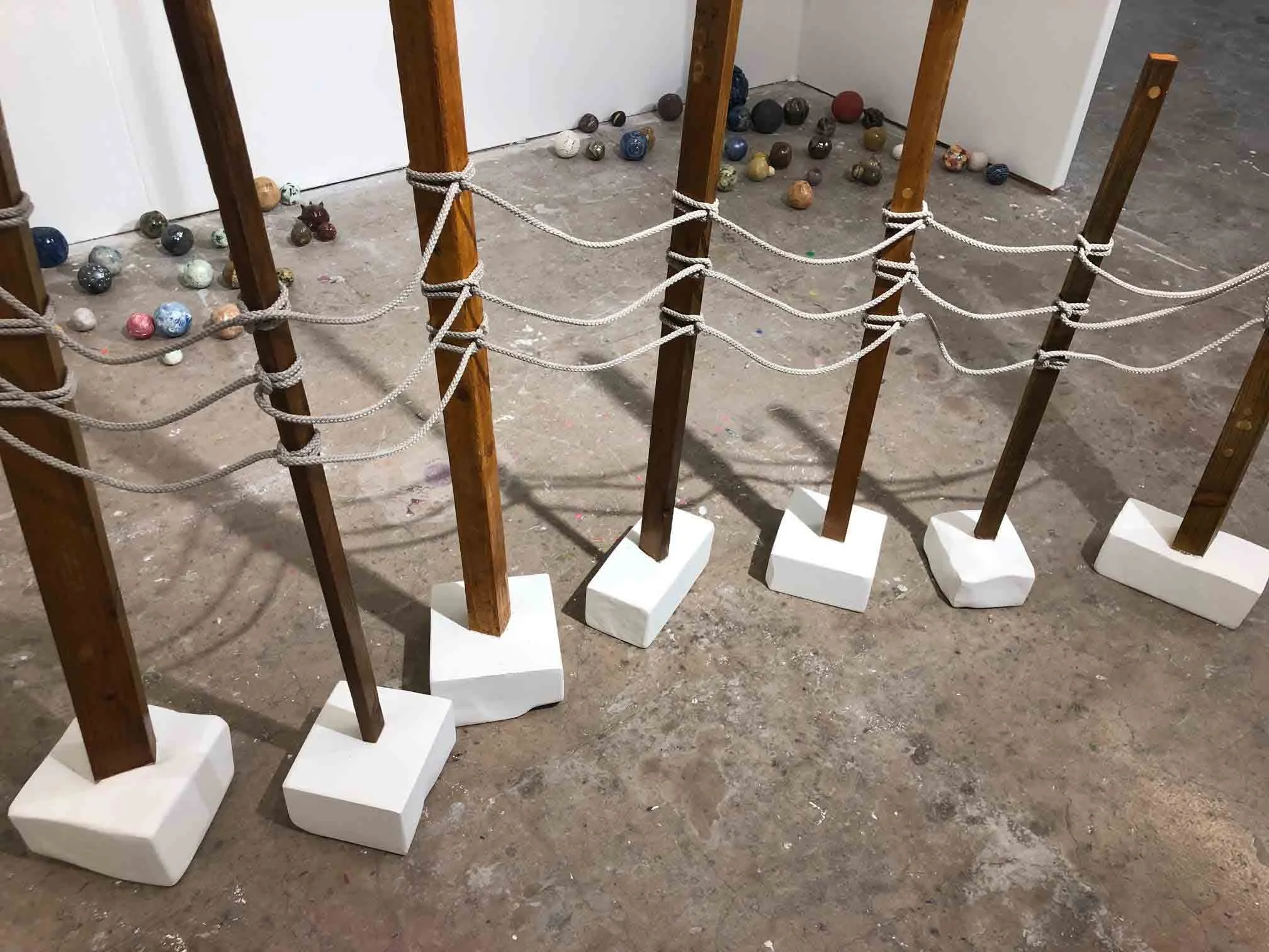 Display of scattered balls behind a wooden and rope barrier on a concrete floor in an indoor space.