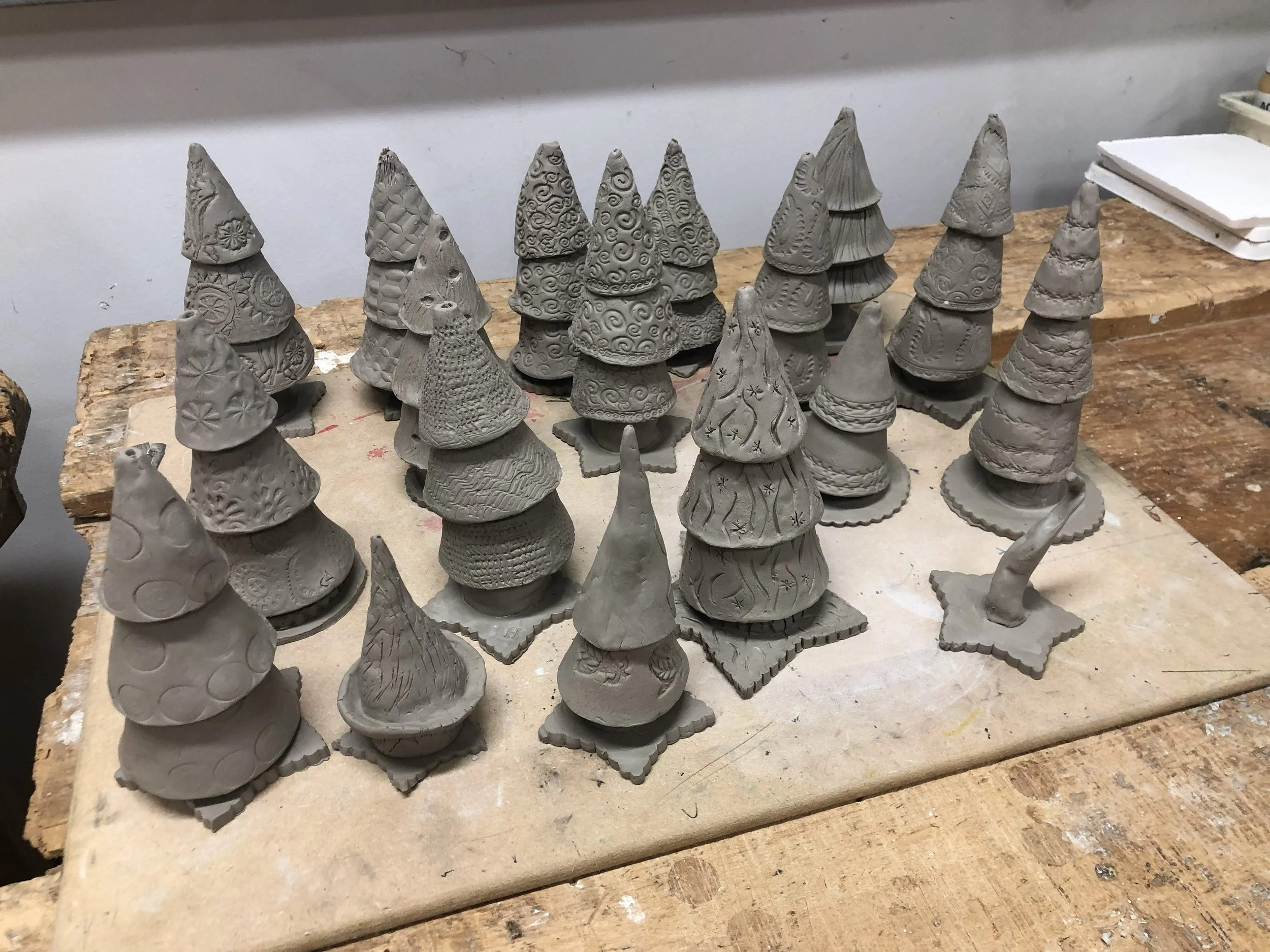 20 unfired, pattern clay christmas trees on a bench