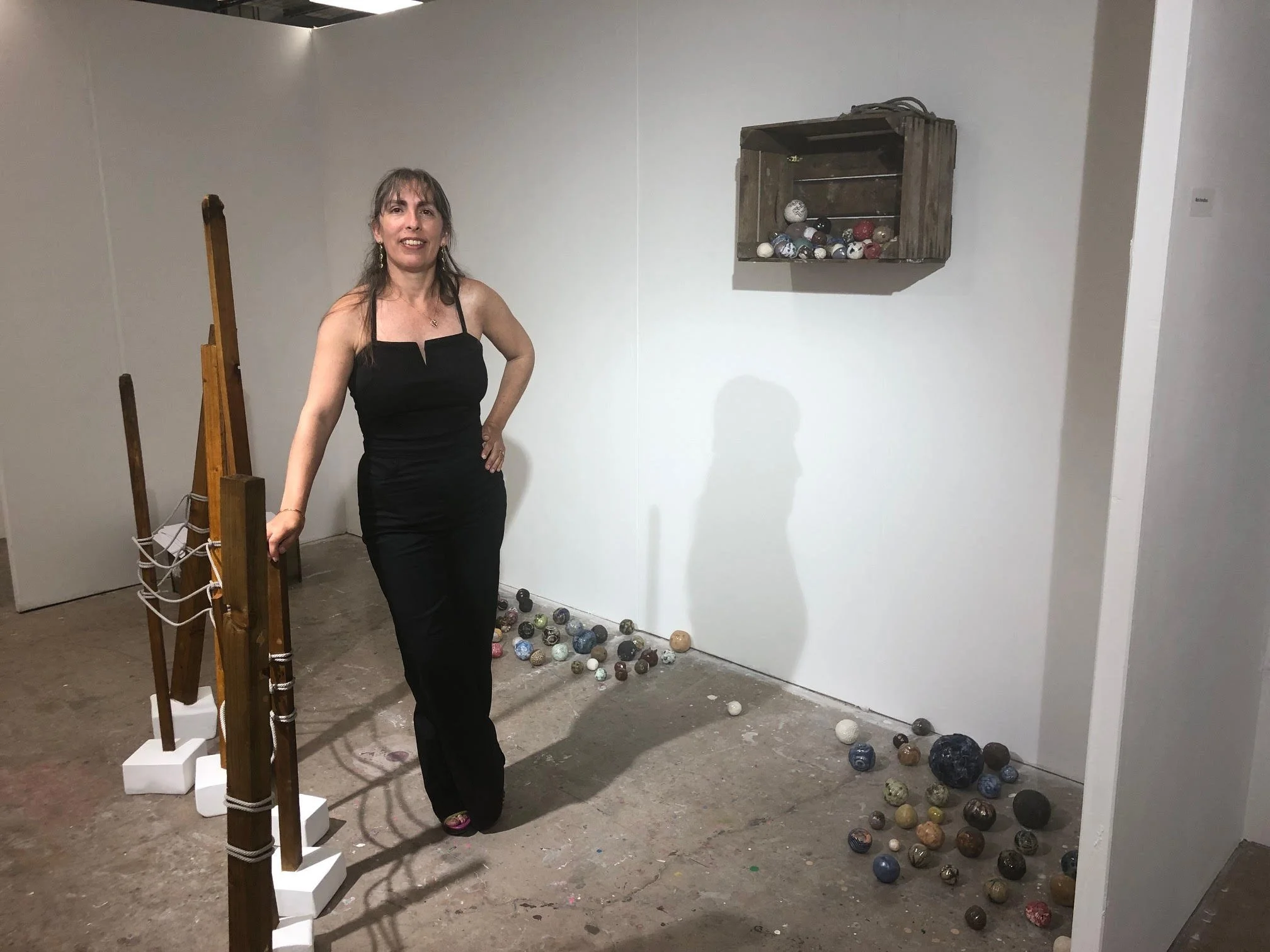 A woman in a black dress standing in art gallery near sculptures and scattered decorative spheres on the floor.