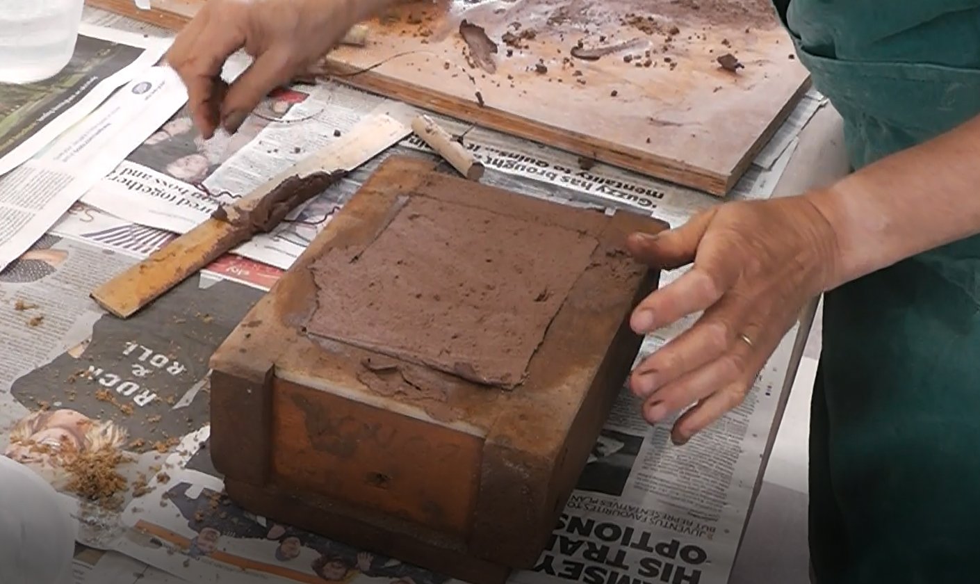 Someone working with a brick and mortar, using a wooden mold on a table covered with newspapers.