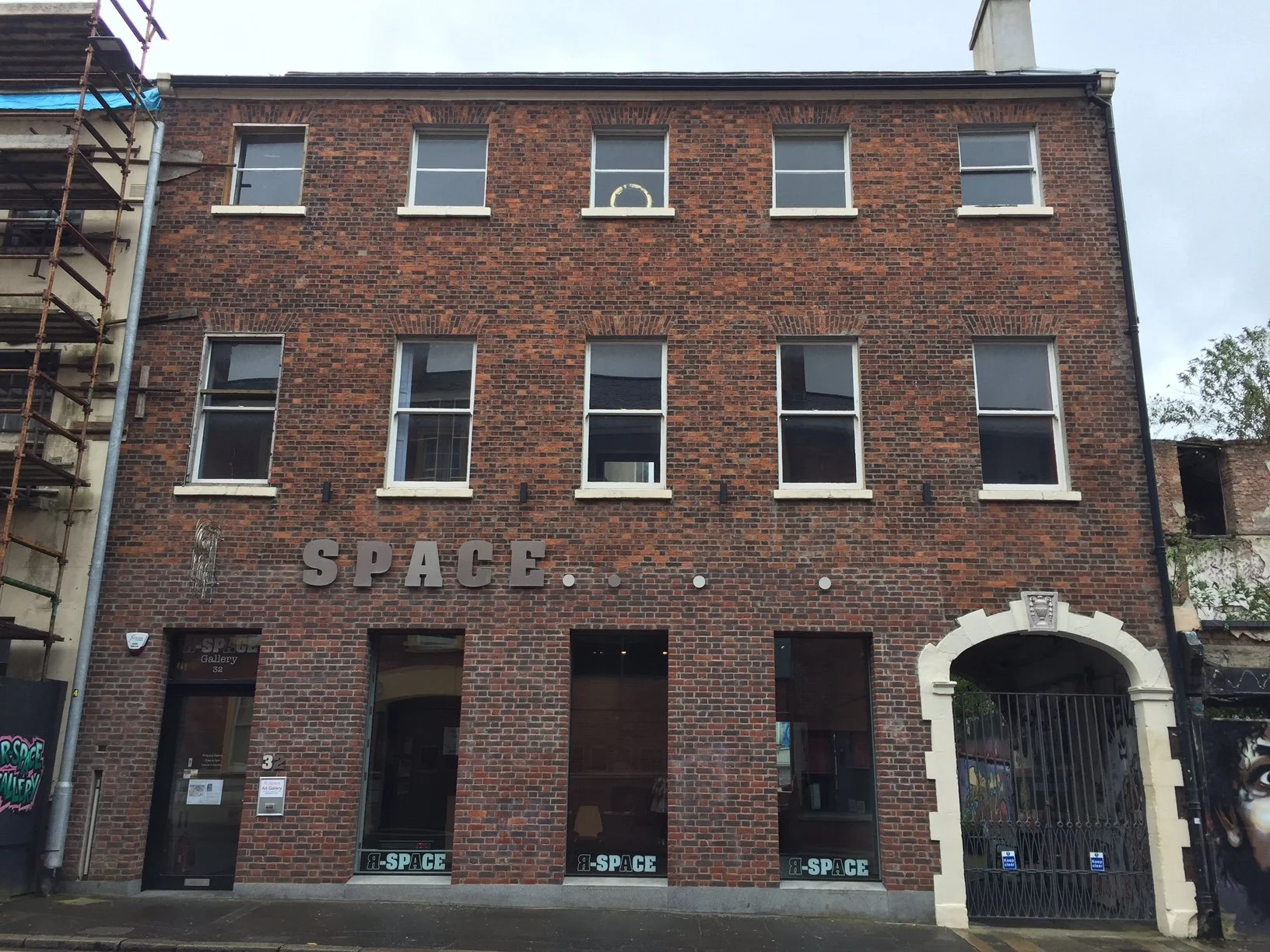 A brick building with the word 'SPACE...' in large letters on the front, with the entrance gate on the right side and four windows on the upper floors.