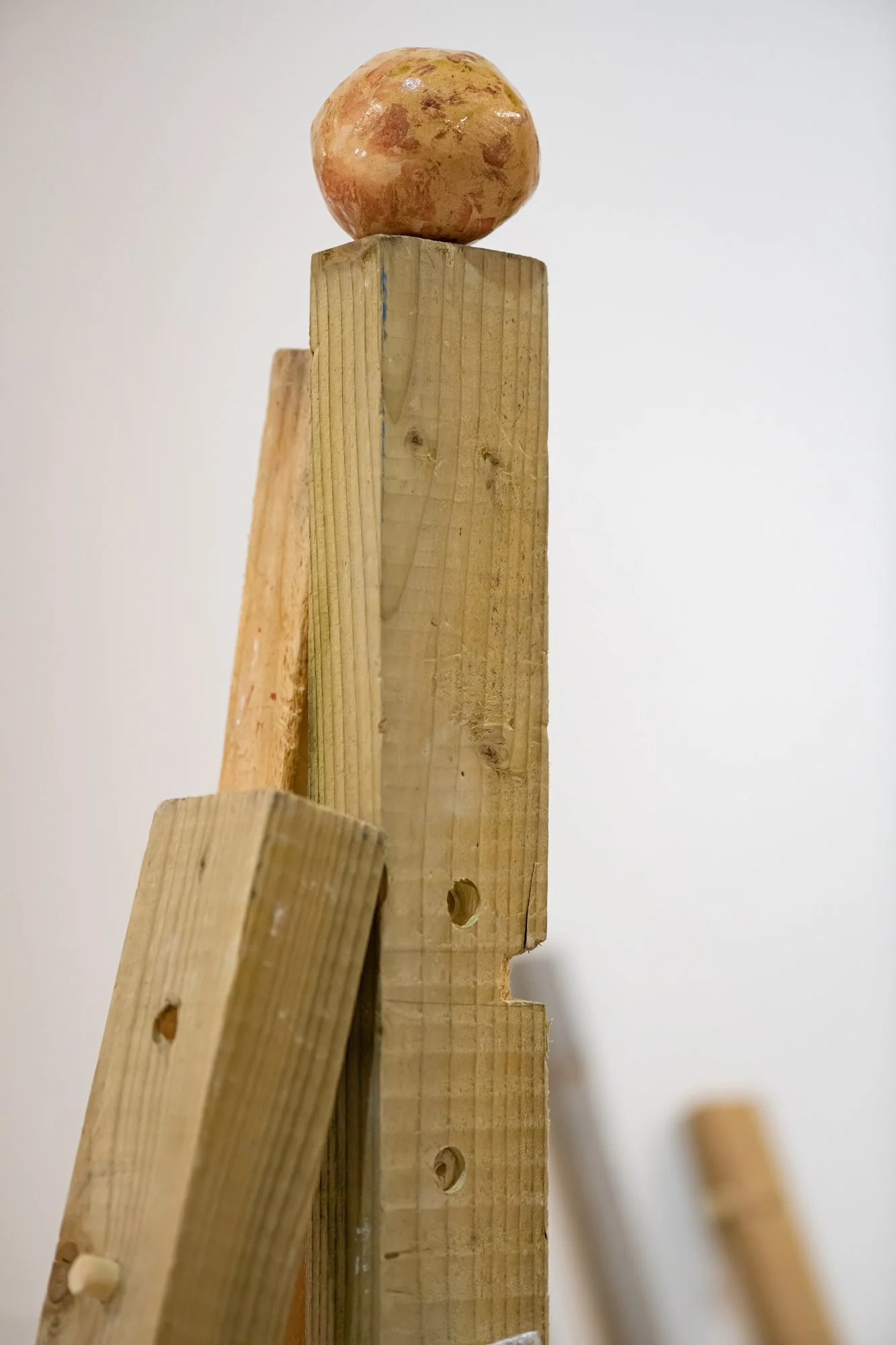 Close-up of wooden pieces stacked vertically, with a small ball on top against a plain white background.