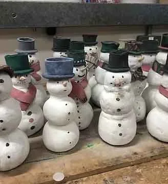 Collection of small snowman decorations wearing hats and scarves, arranged on a wooden surface.