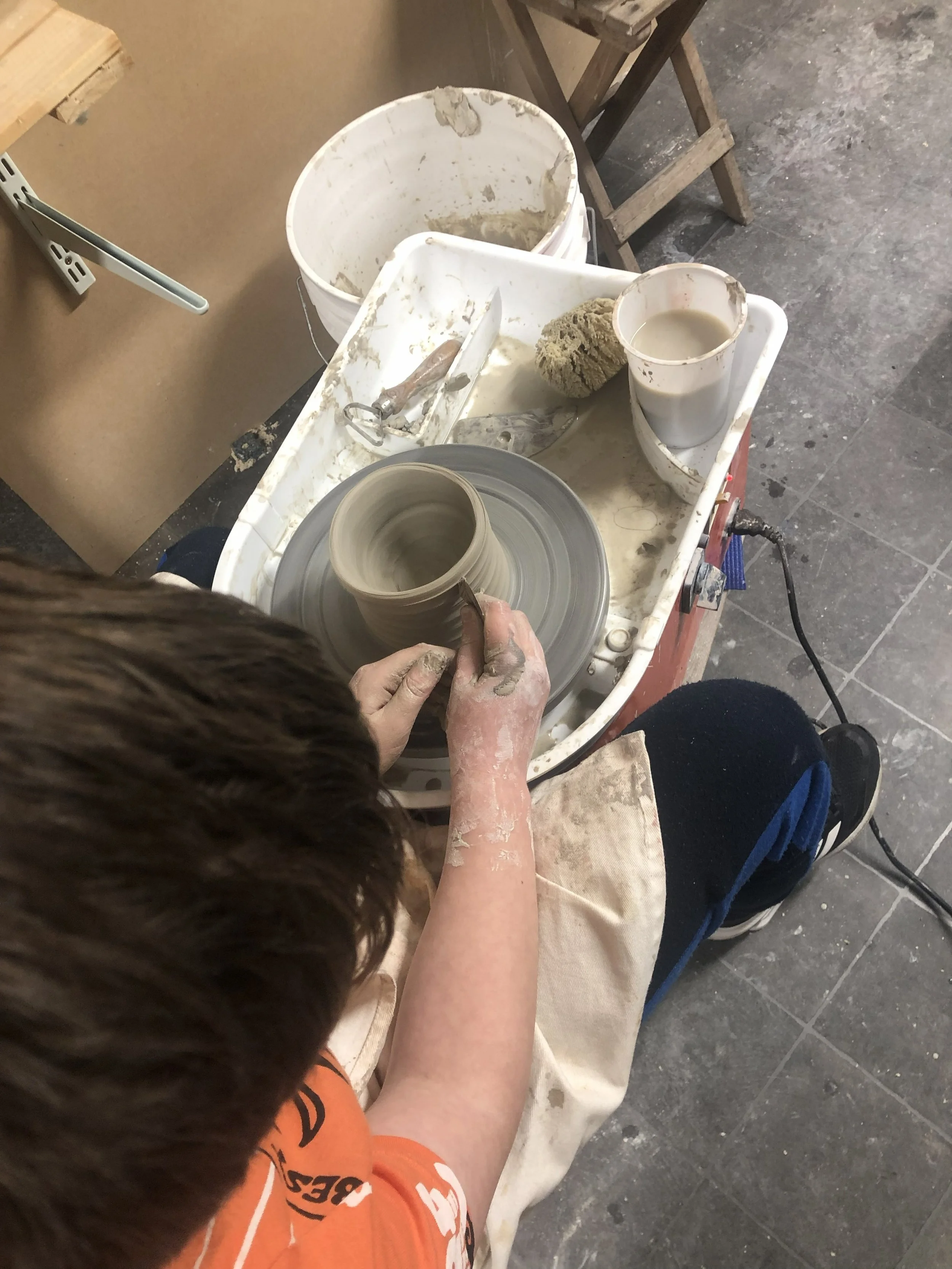 young man throwing on a kid size pottery wheel