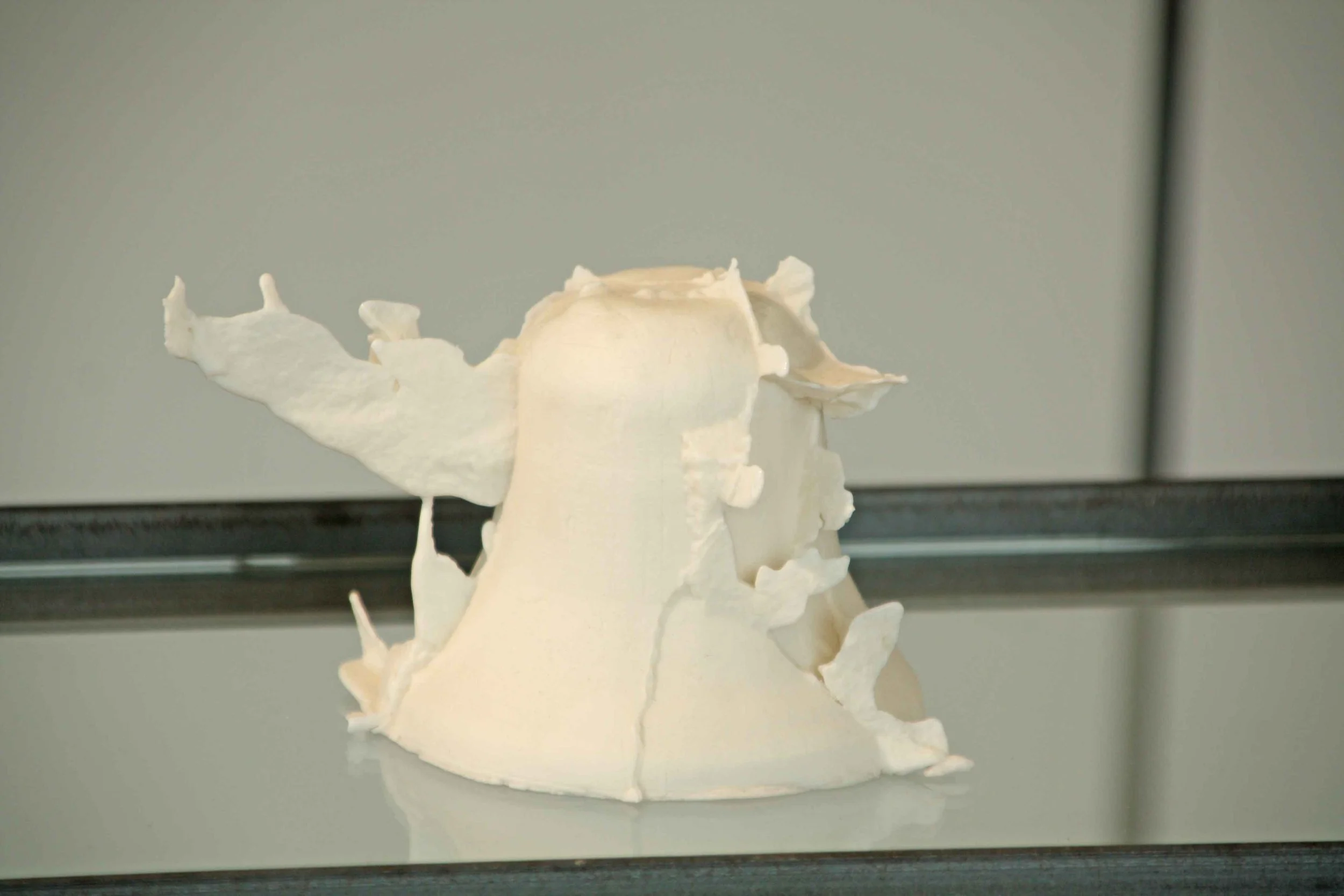 A white sculptural art piece resembling a bird or abstract form on a black surface against a plain background.