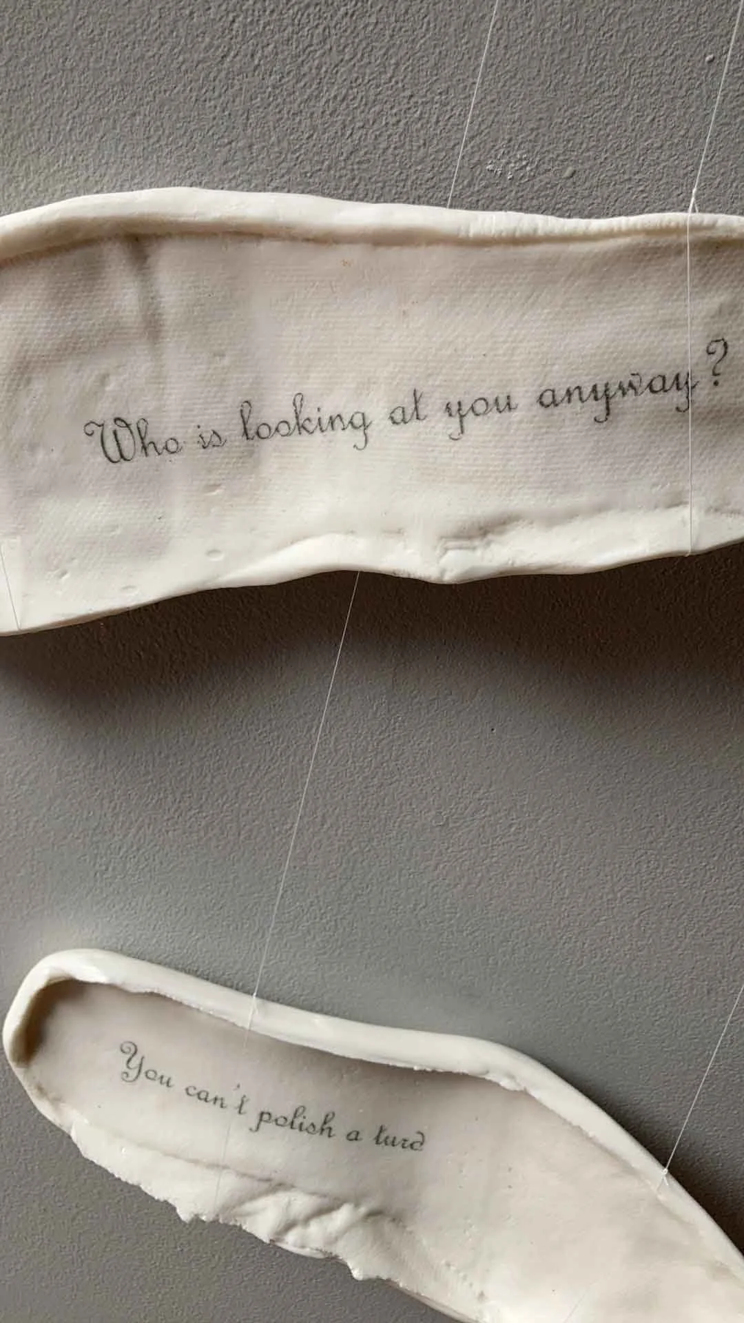 Close-up of white ceramic soles with embroidered or printed text, one asking 'Who is looking at you anyway?' and the other partially visible with the words 'You can't polish a turd.'