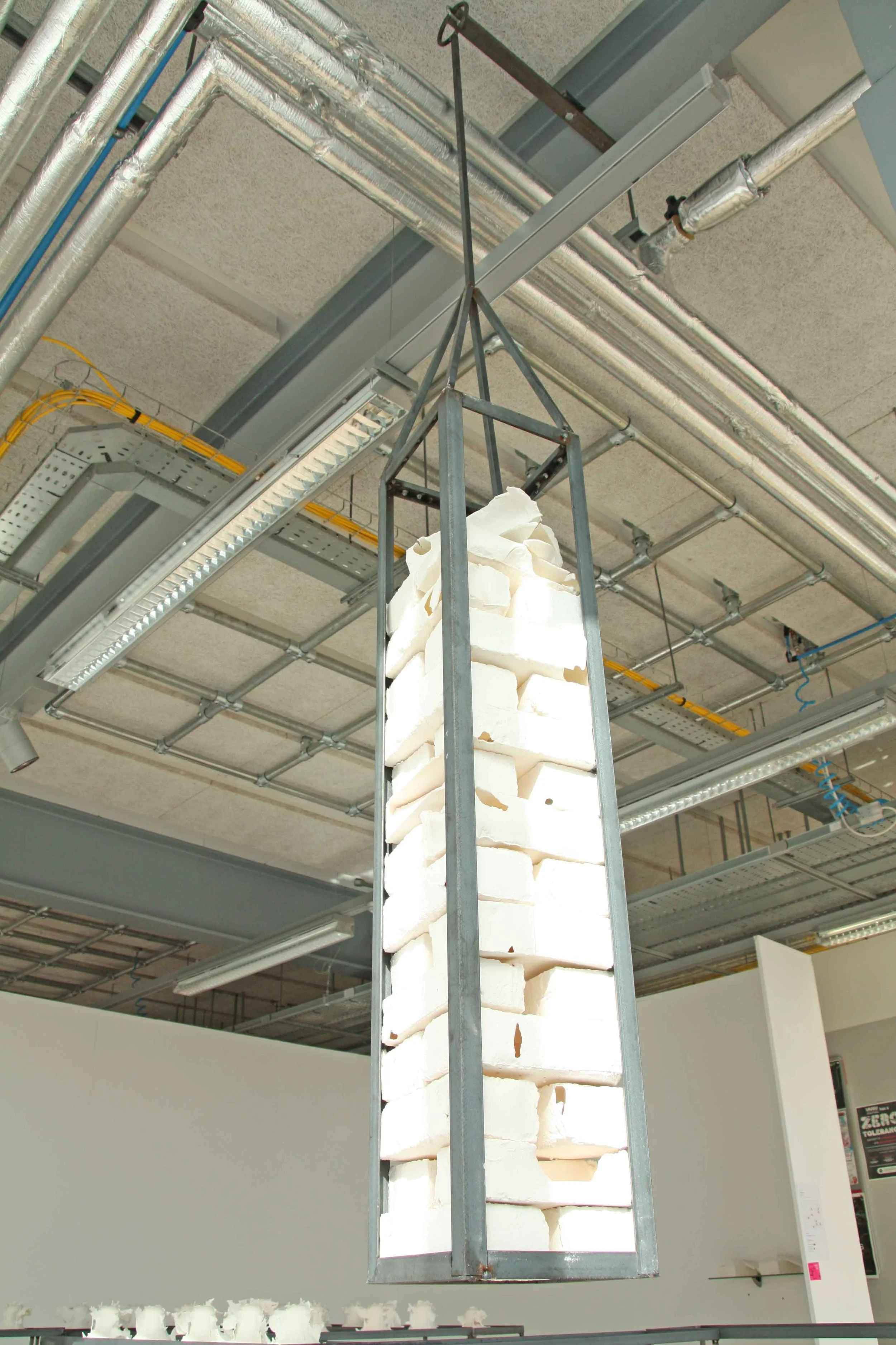 A large pile of white ceramic bricks inside a metal cage hanging from the ceiling in a building under construction.