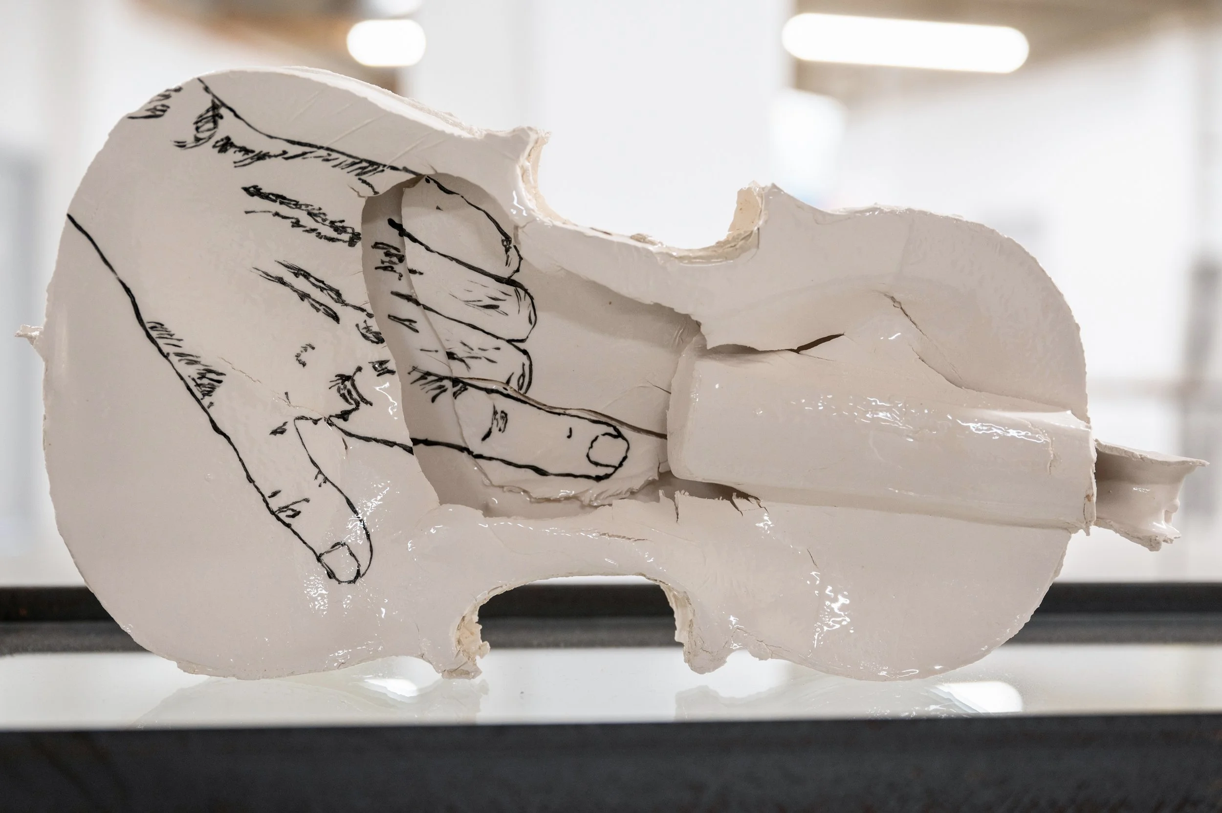 Sculpture of  white porcelain violin with a line drawn hand drawn on it, the pointed finger where the porcelain is broken