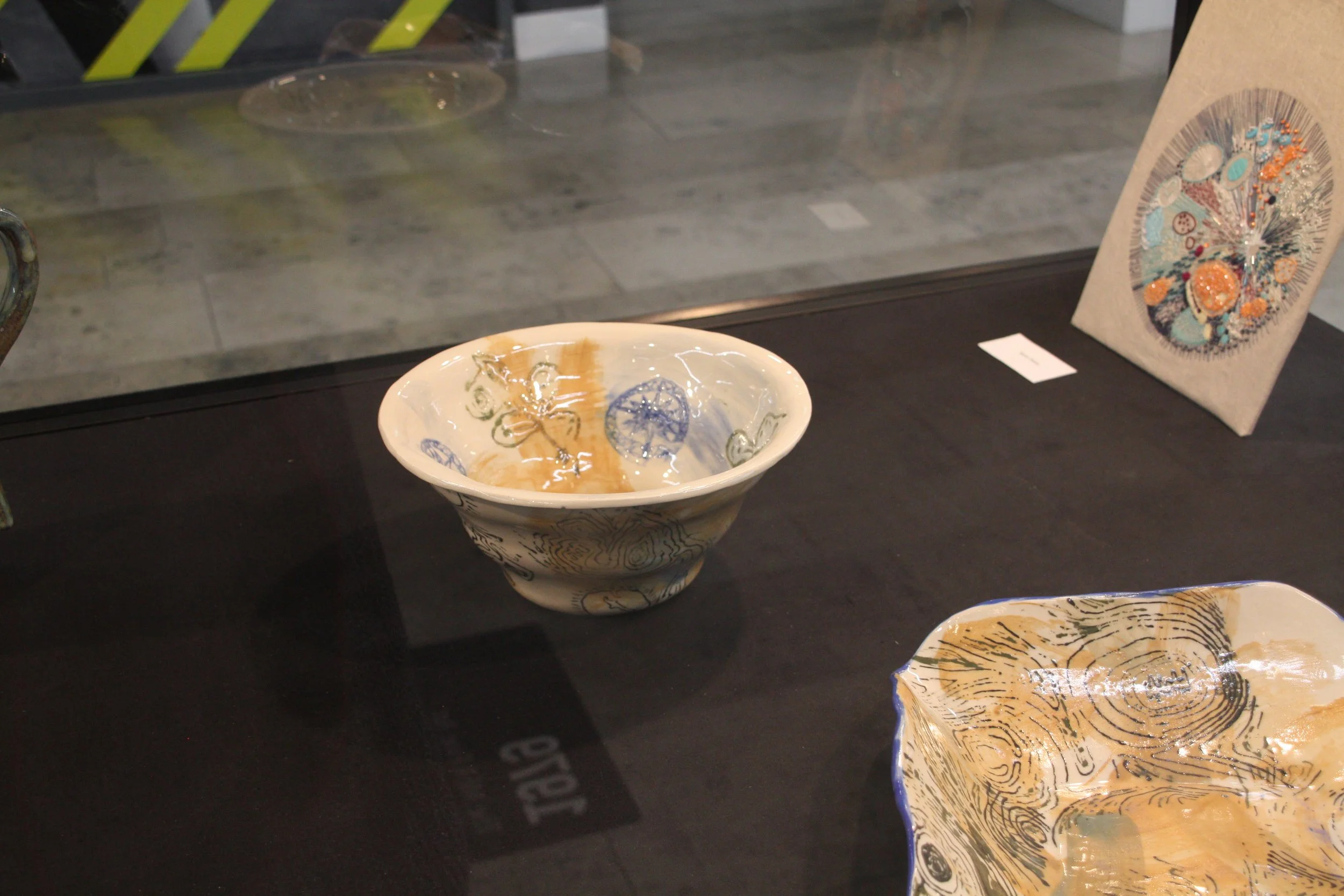 Decorative ceramic bowls with intricate patterns and illustrations on display on a black surface, with other ceramic pieces visible in the background.