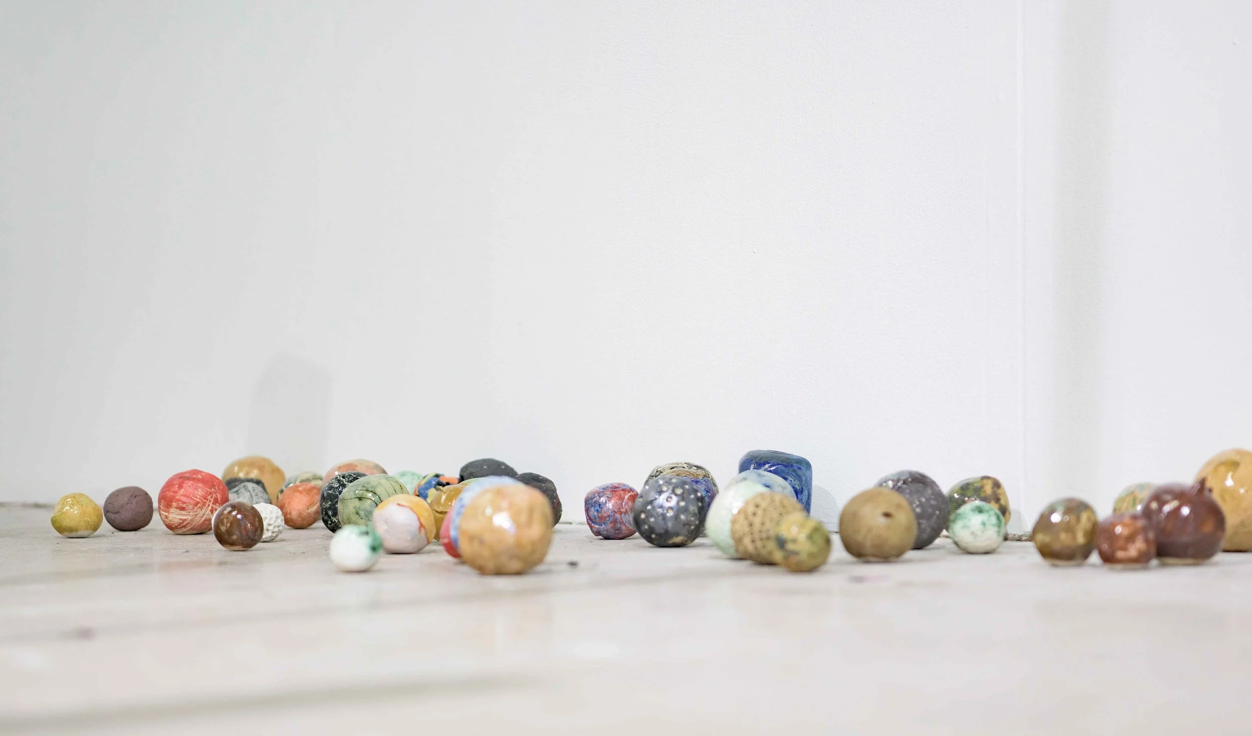 A collection of small, colorful, handmade ceramic or clay balls scattered on a flat surface against a plain white wall.