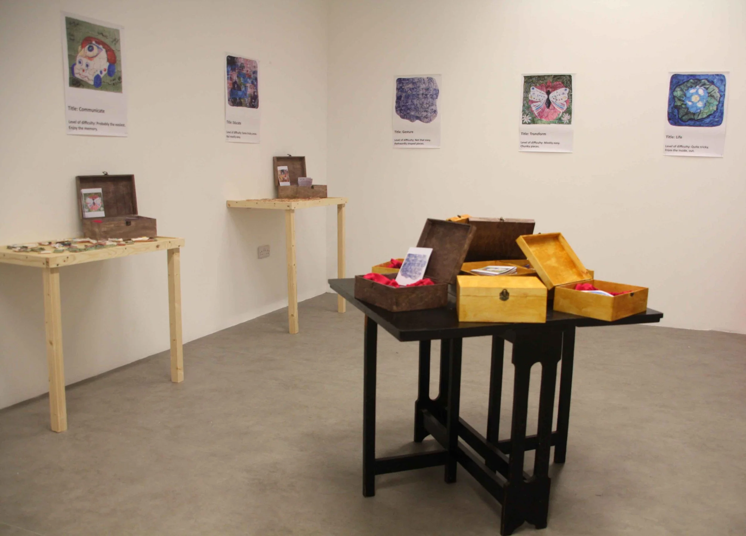 Gallery wall with paintings and descriptions, display tables with boxes and items, and a small stand with informational material.