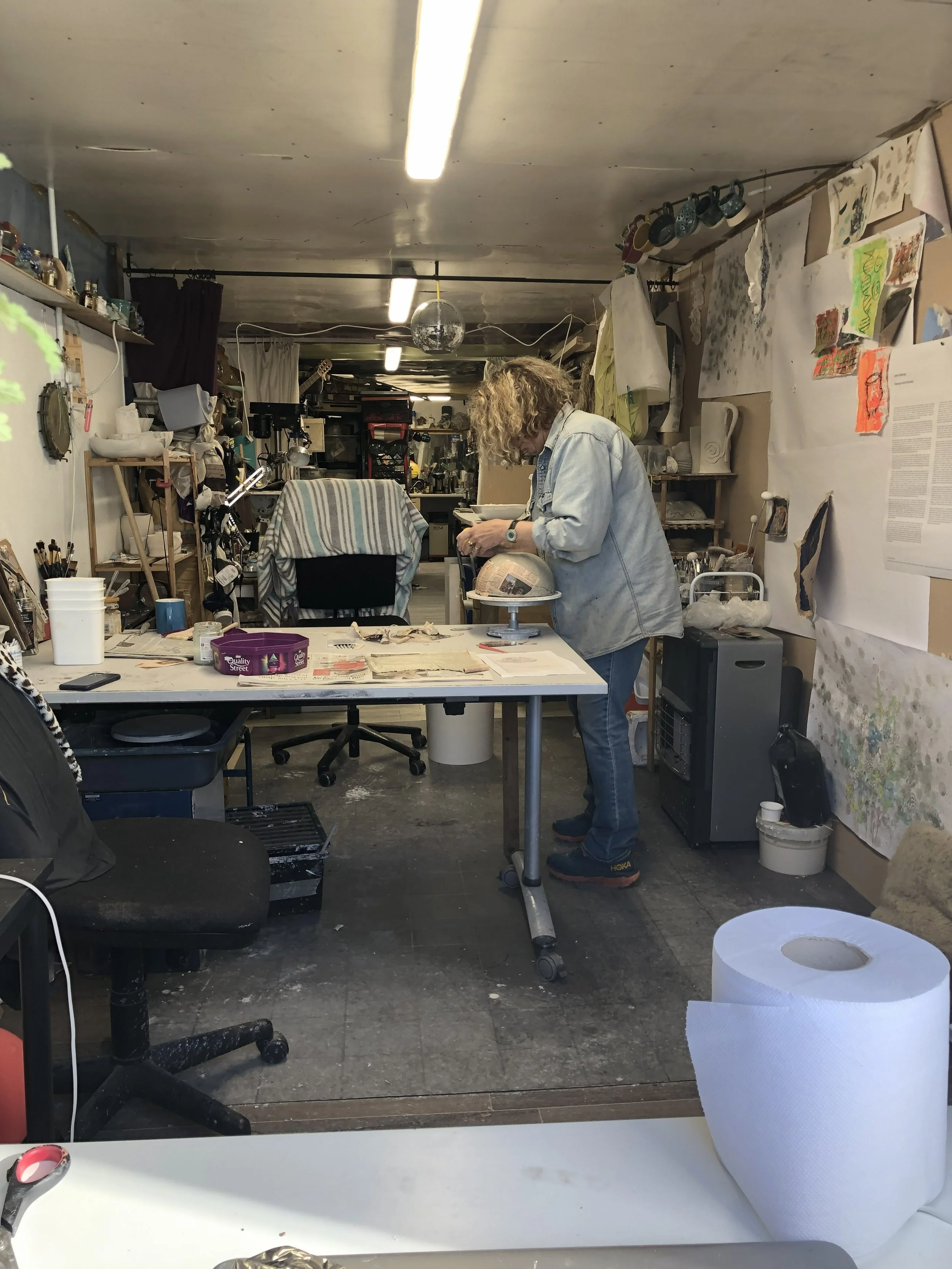 art studio with a woman with messy curly hair working at a table on clay