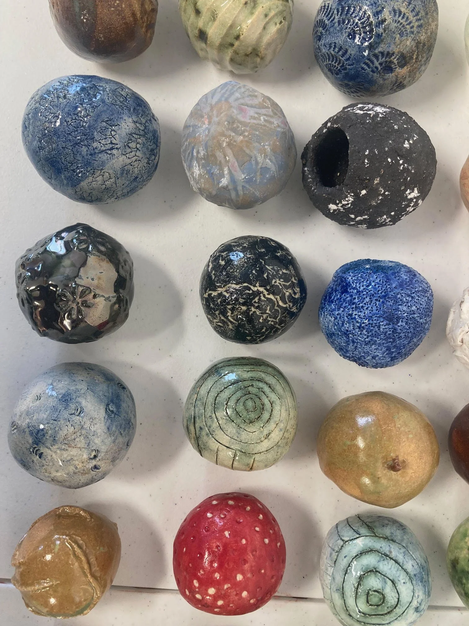 Collection of various decorative ceramic and glass spheres with different textures, colors, and patterns arranged on a white surface.