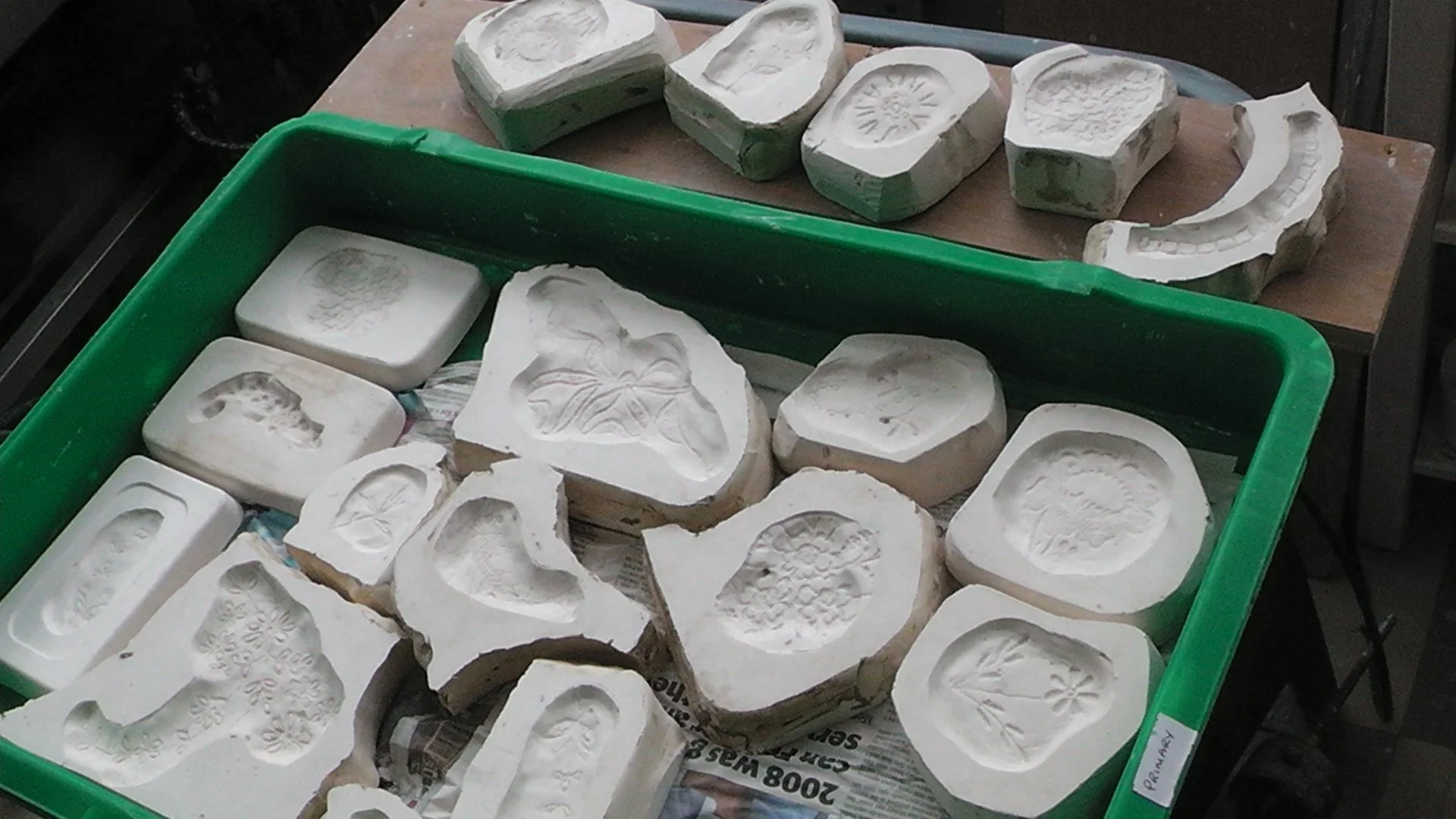 Silicone mold forms with floral and abstract patterns on a table, some in a green plastic container, used for creating decorative items or crafts.