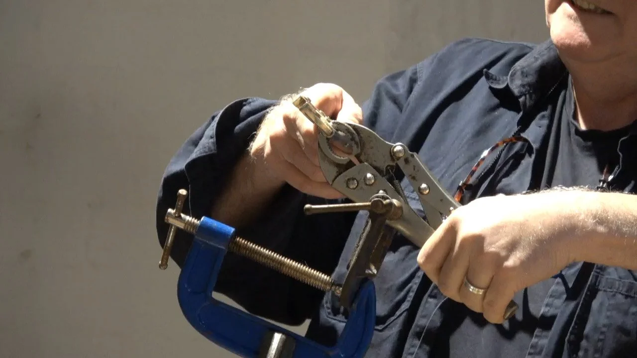 A person using a pair of locking pliers to hold a small object, with a blue clamp securing a metal rod or pipe.
