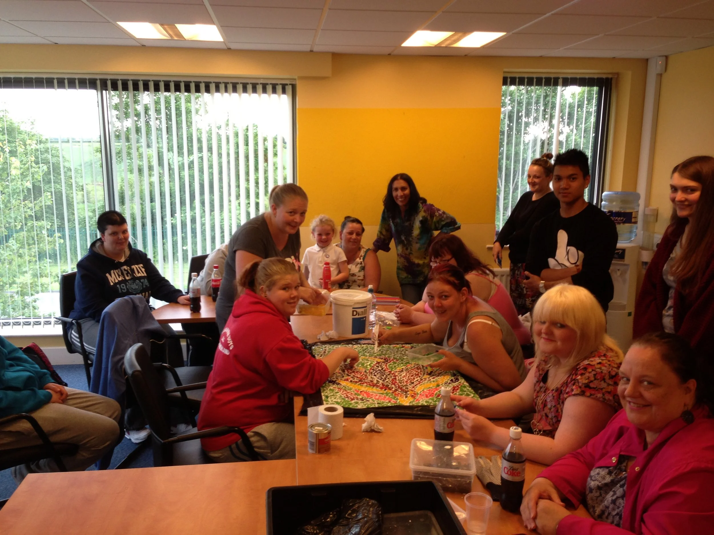 Group of people gathered around a table in a room with large windows, some smiling and looking at the camera.