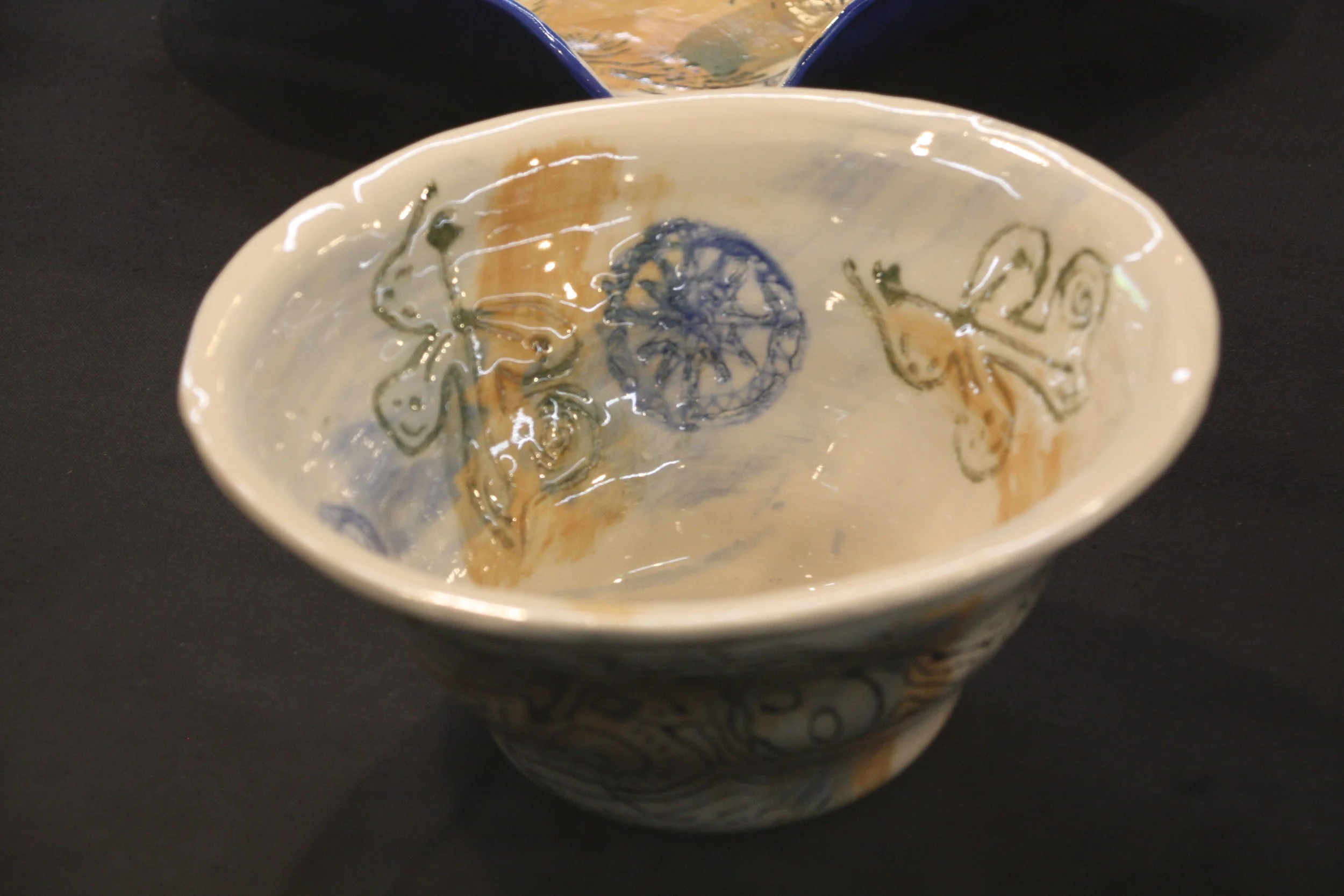Decorative ceramic bowl with blue and beige designs, partial view, placed on a black surface, with a second bowl visible in the background.