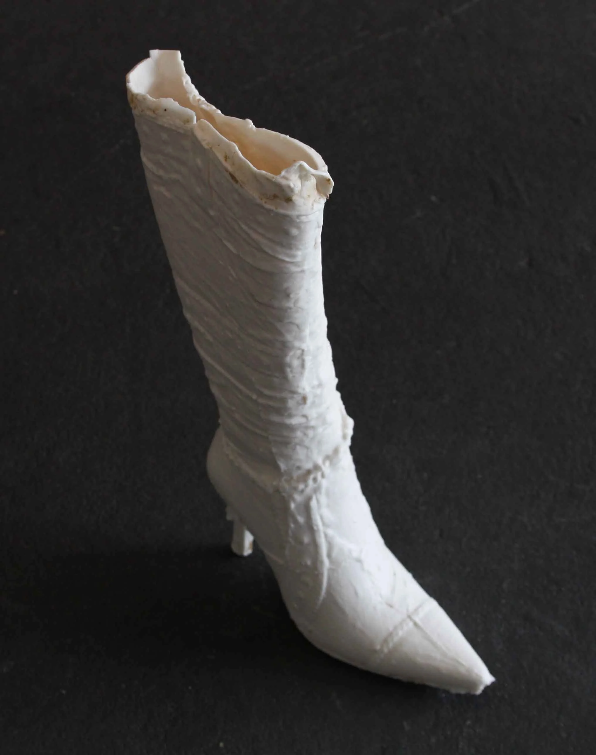 cast ceramic stiletto boot standing upright on a dark floor